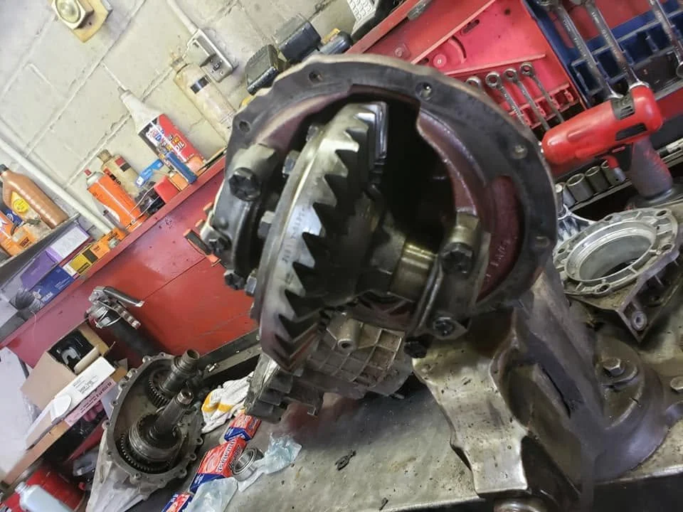 Close-up of an engine component removed from a vehicle, on a workbench with tools and parts in a garage or workshop.