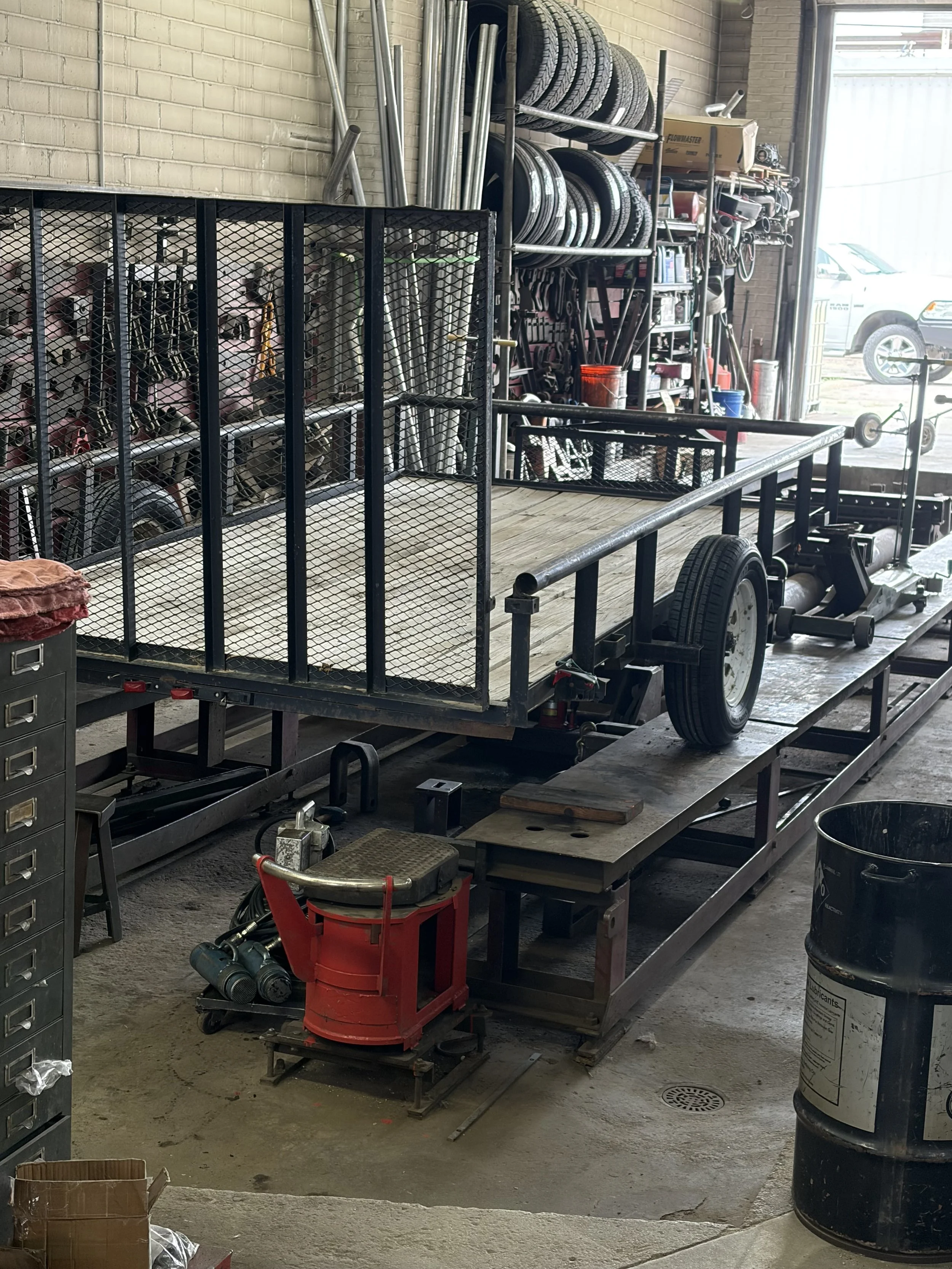 Inside an auto workshop with a flatbed trailer, car tires on shelves, various tools, and equipment.