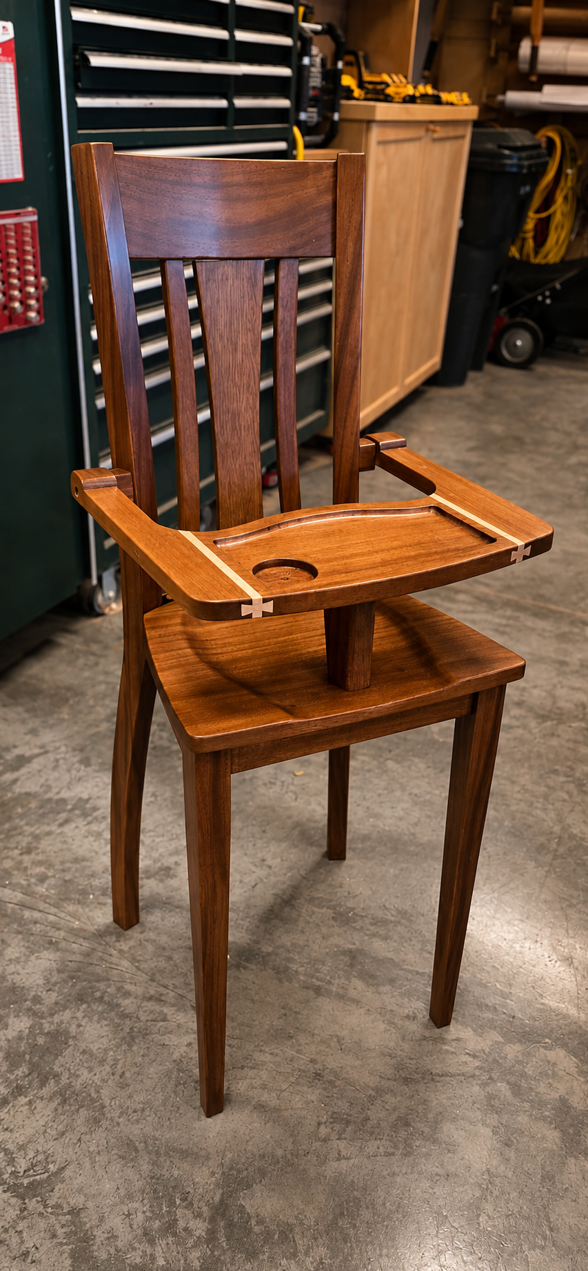A wooden chair with an attached high chair tray and cup holder, inside a workshop or garage setting.