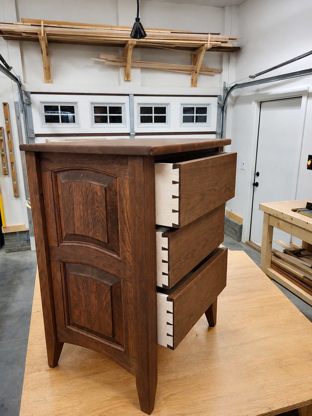 Wooden dresser with three drawers, partially open, in a woodworking shop.