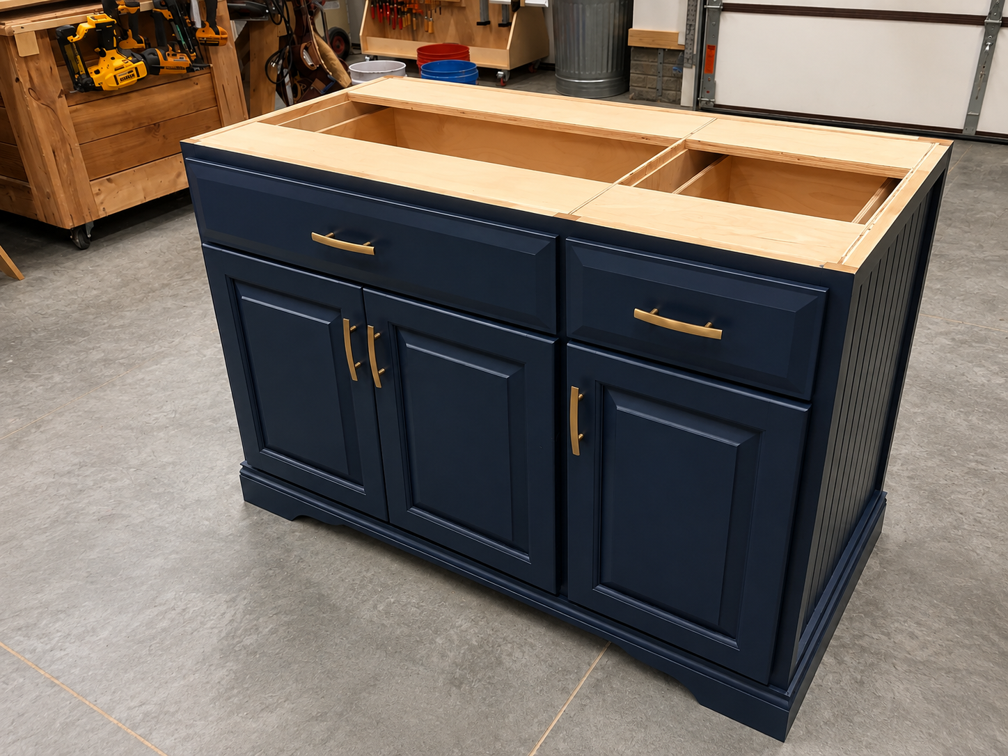 A partially assembled kitchen cabinet with dark blue paint and gold handles, situated in a workshop against a gray floor.