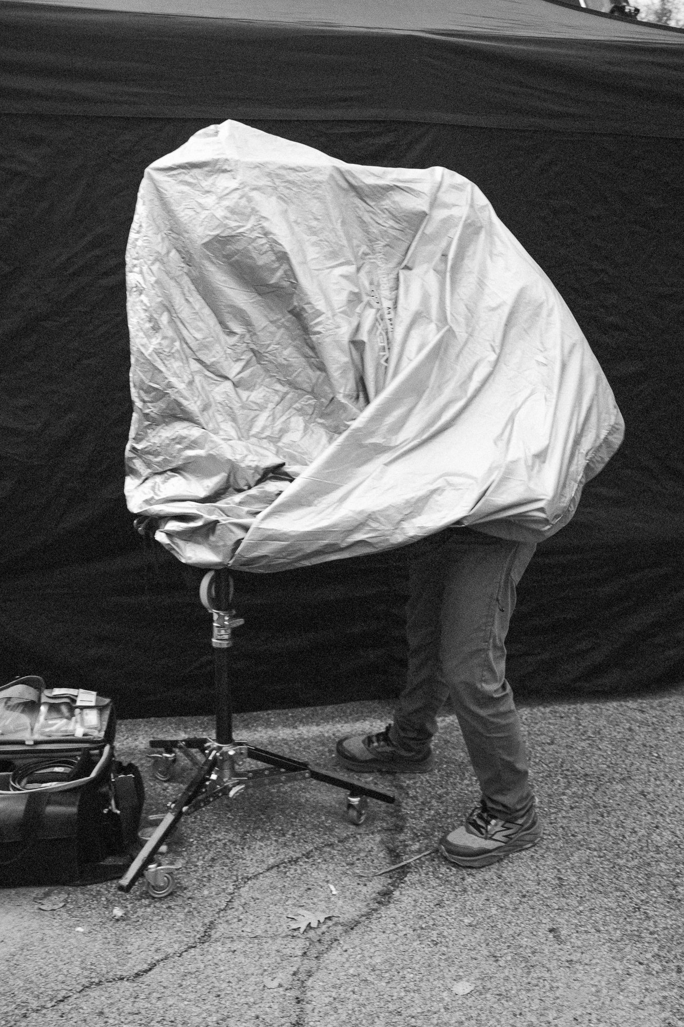 Person standing next to a covered bicycle or object, with bicycle tools and equipment nearby, outdoors on a paved surface.