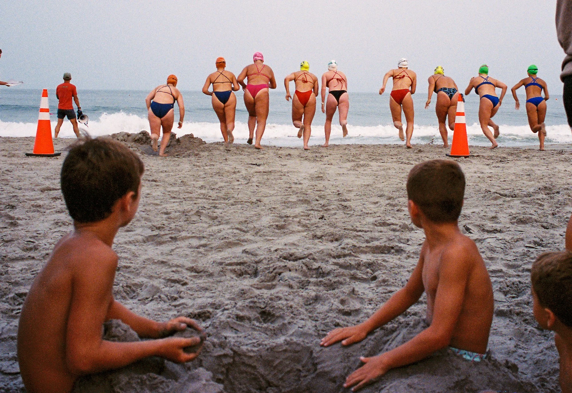 Children and adults at a beach, some sitting and some running into the water.