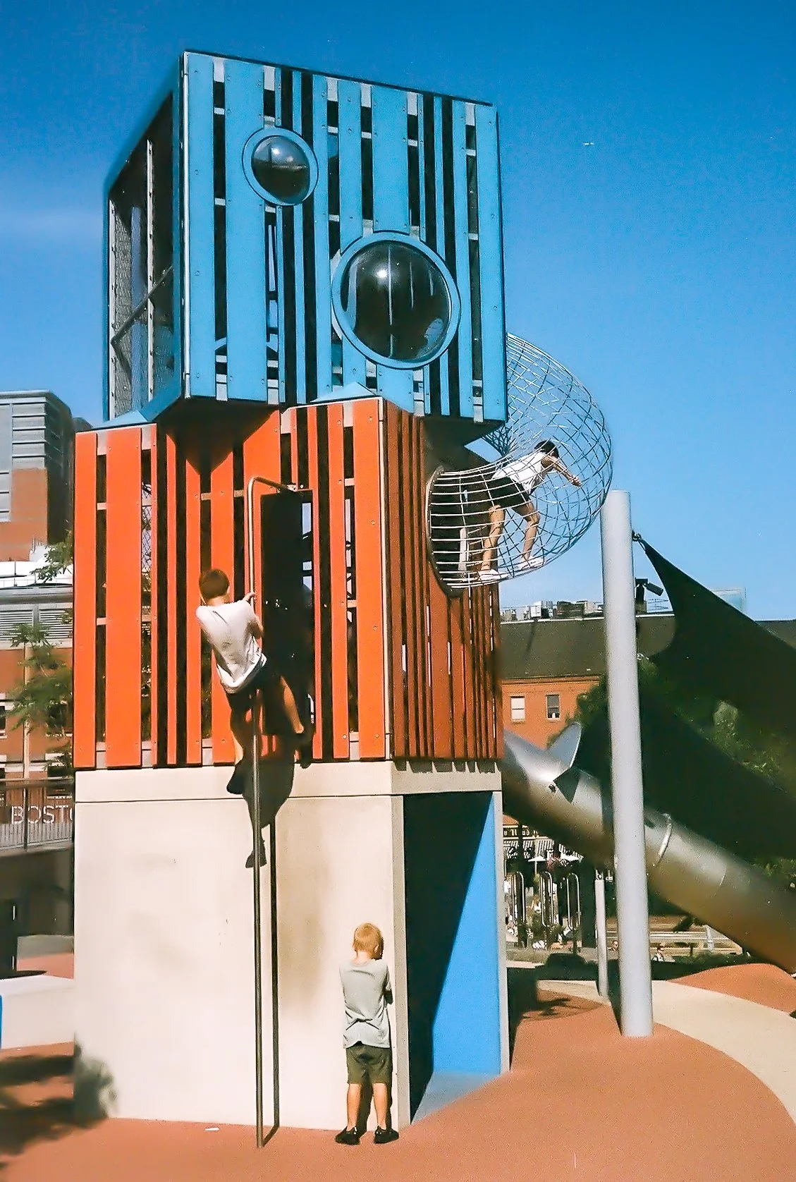Children playing on colorful modern playground structure with slides and climbing areas against clear blue sky.