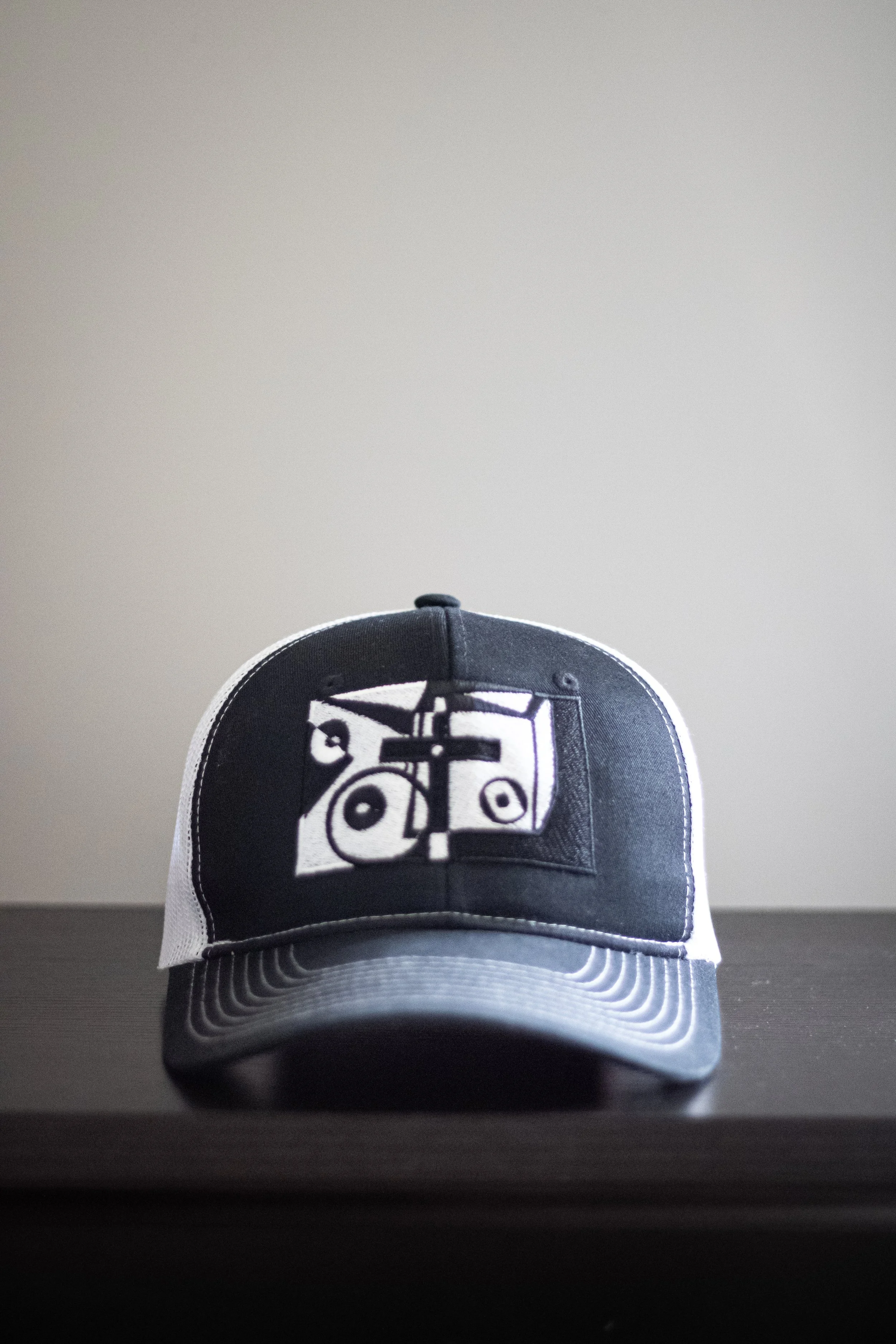 Black and white baseball cap with a graphic logo on the front, placed on a flat surface against a plain background.