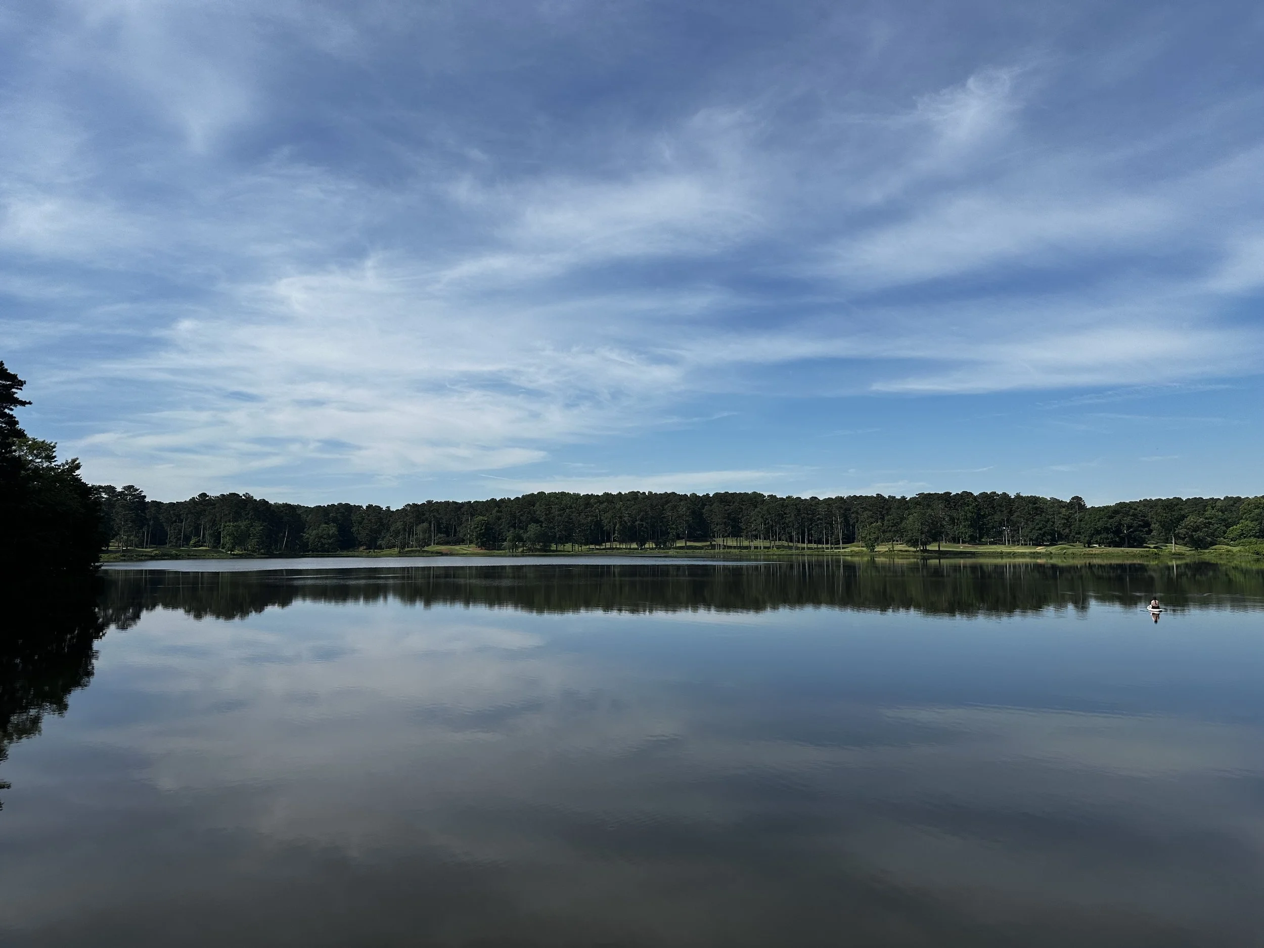Calm Lake Allatoona reflecting a blue sky with scattered clouds, surrounded by a forested shoreline with trees in Acworth, GA.