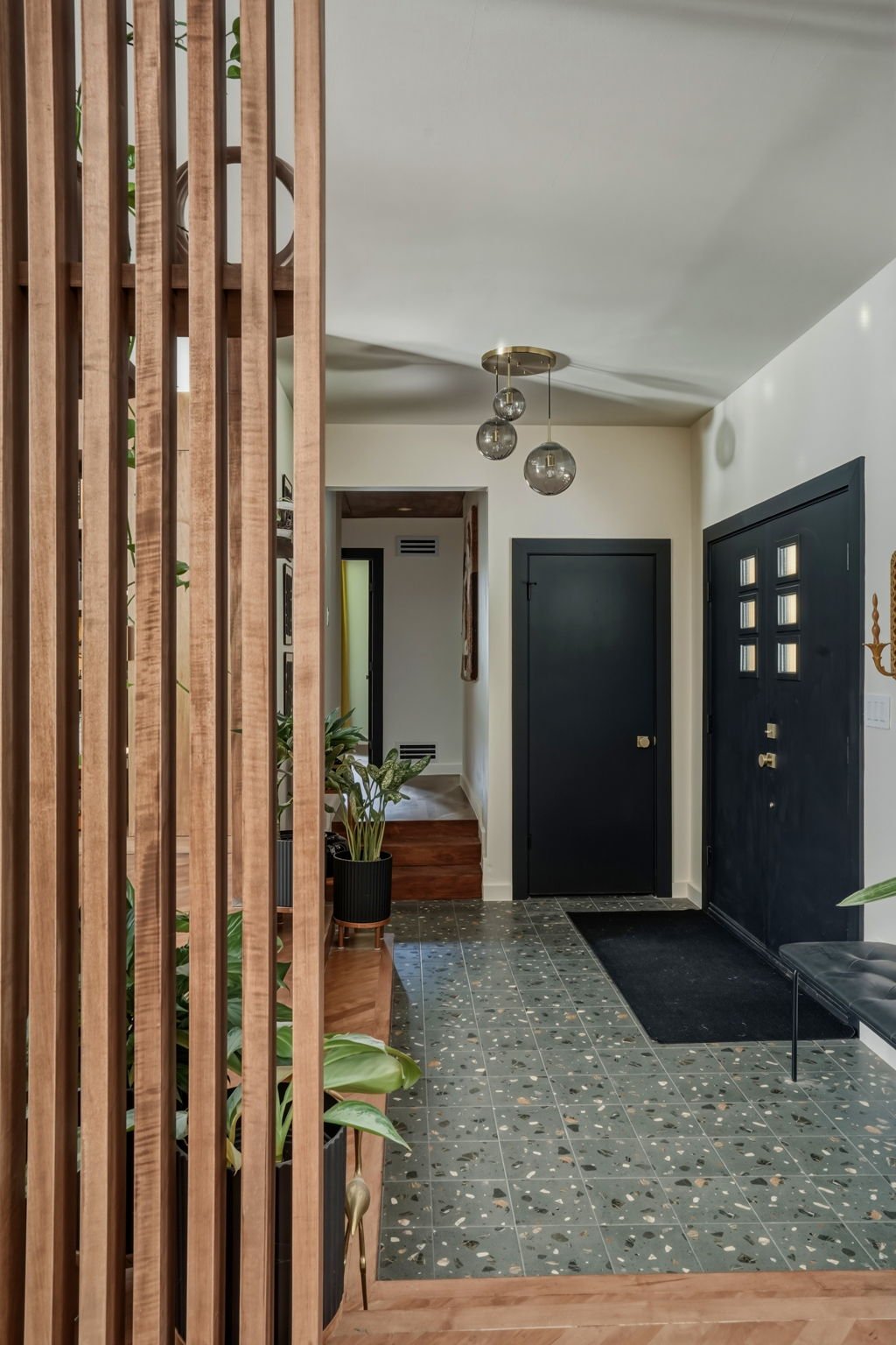 Modern entryway with black door, terrazzo flooring, wooden slat wall, hanging pendant lights, and potted plants in Smyrna, GA.