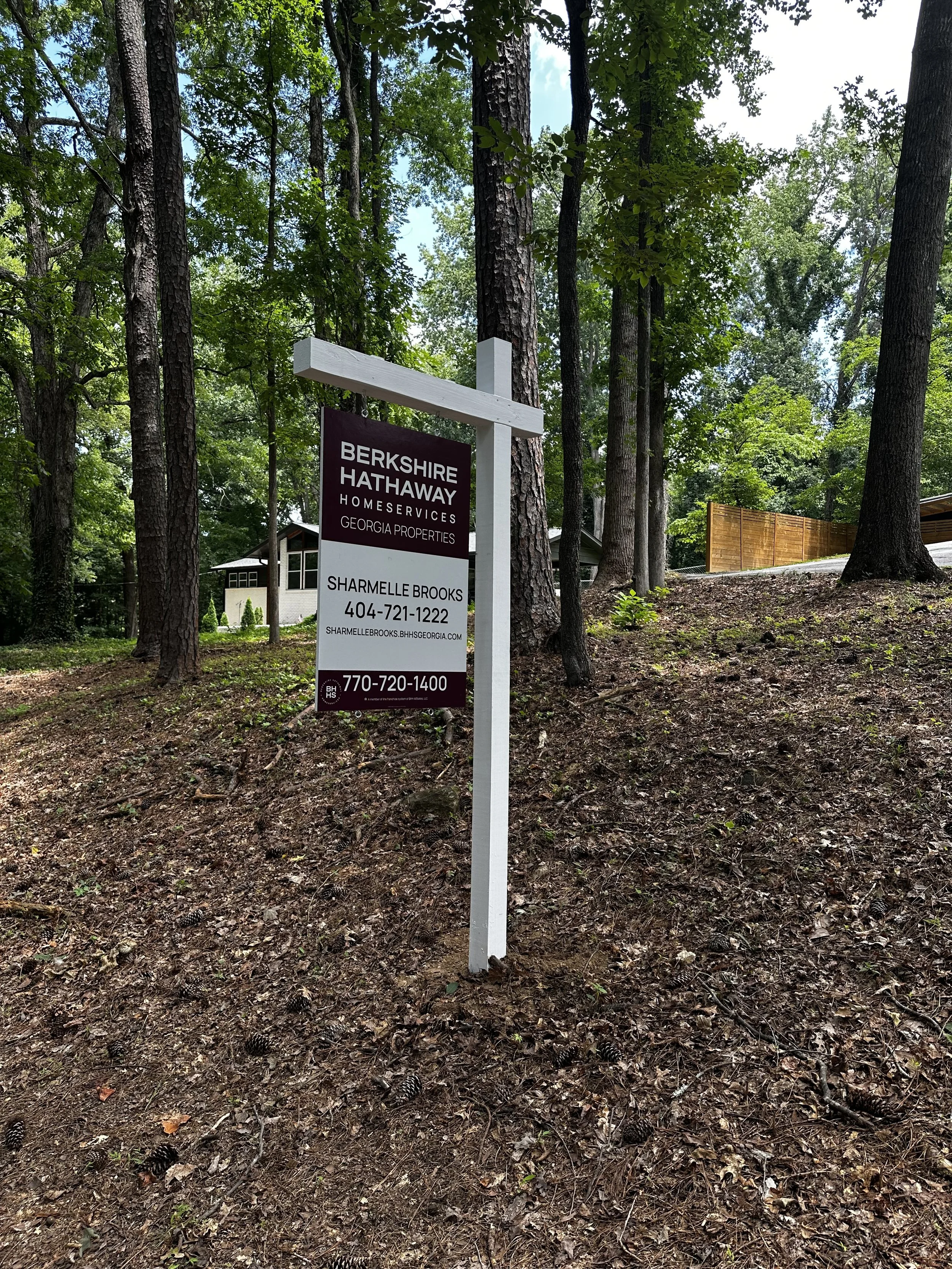 Sharmelle Brooks's Berkshire Hathway HomeServices Georgia Properties yard sign in front of a wooded area with trees, a house, and a fence visible in the background in Smyrna, GA.