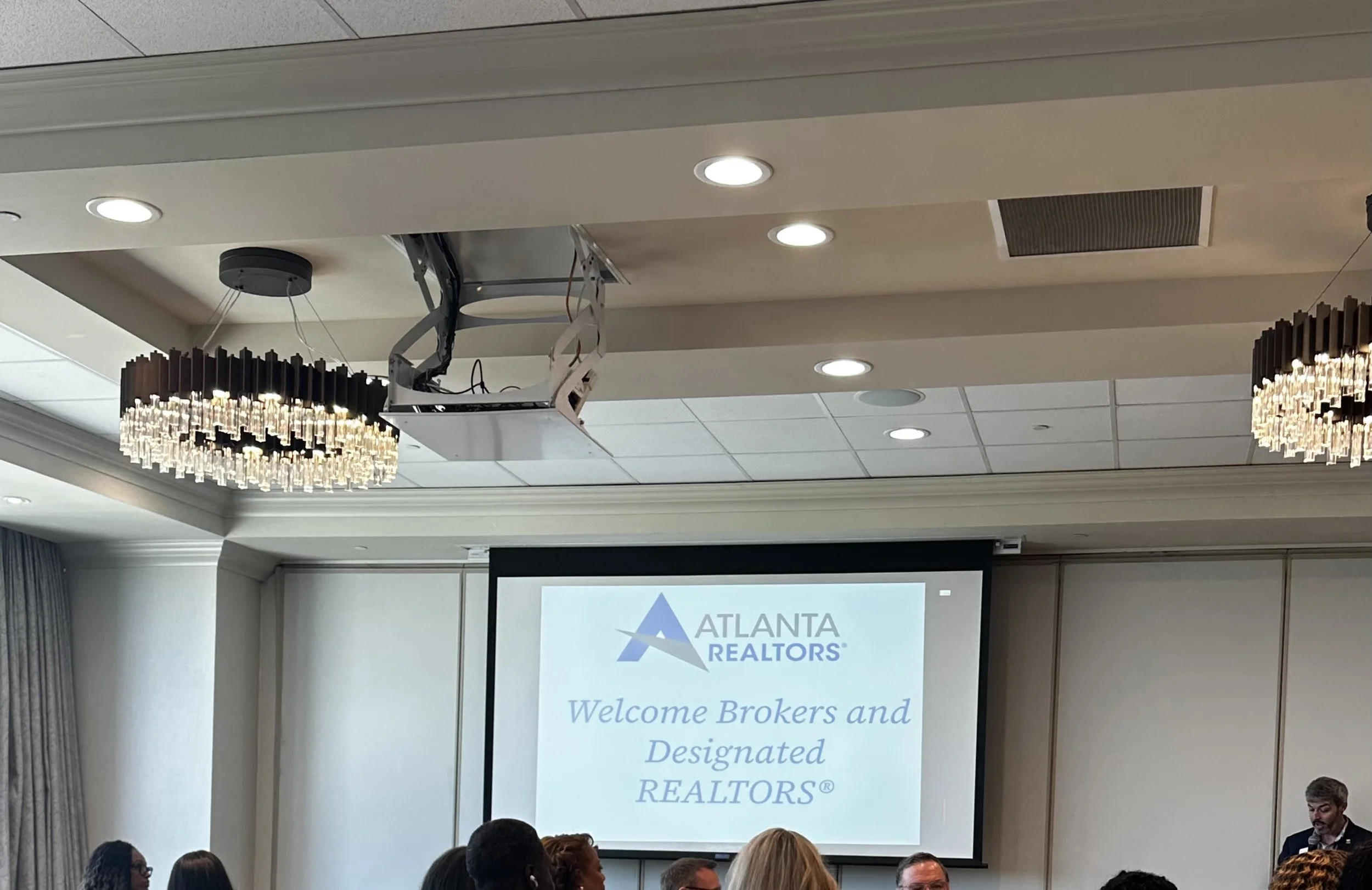 A conference room with people attending a presentation. The screen displays the logo and text of Atlanta Realtors.
