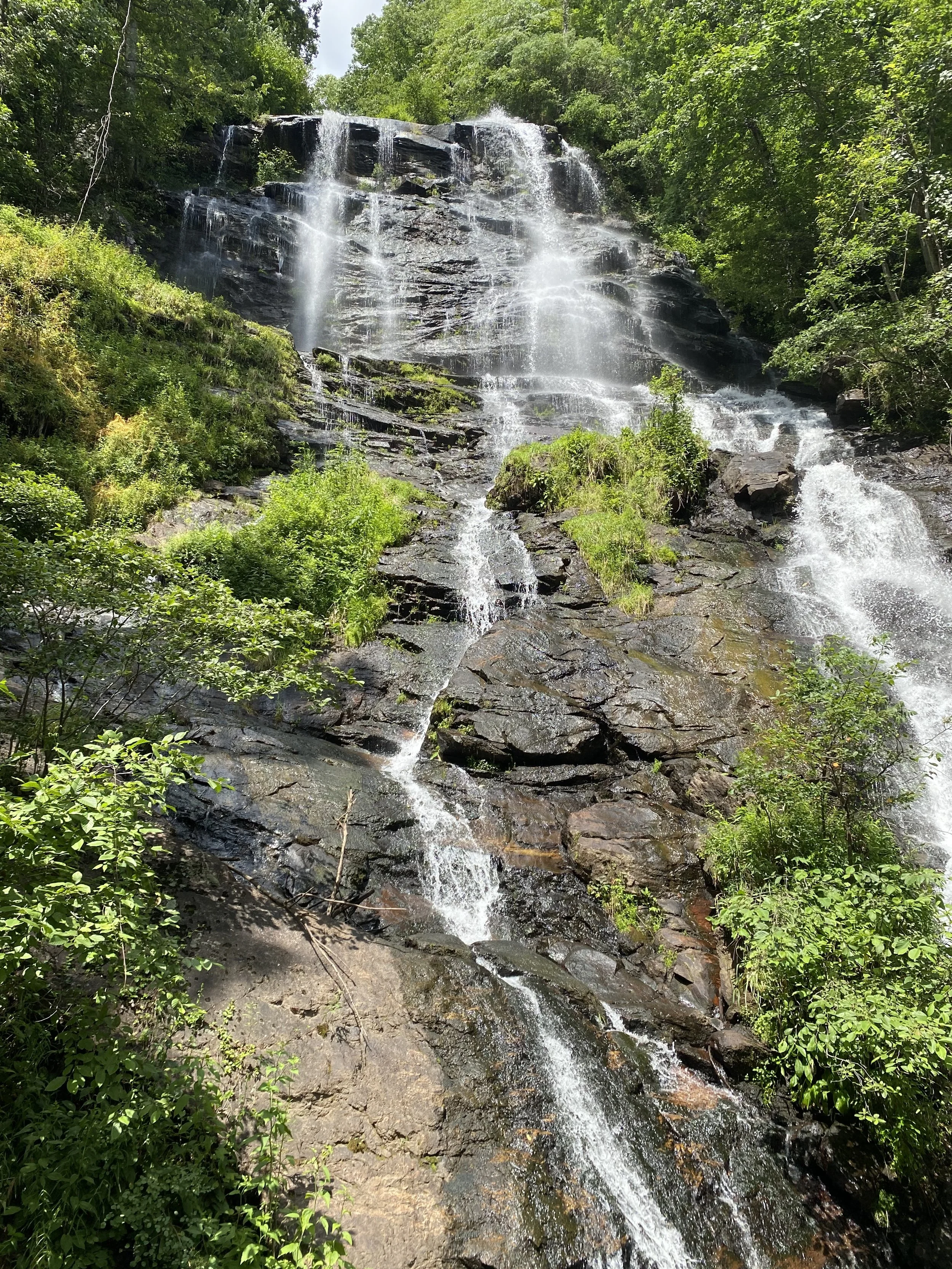 A waterfall flowing down over rocks surrounded by lush green trees and foliage in Amicalola Falls, GA.