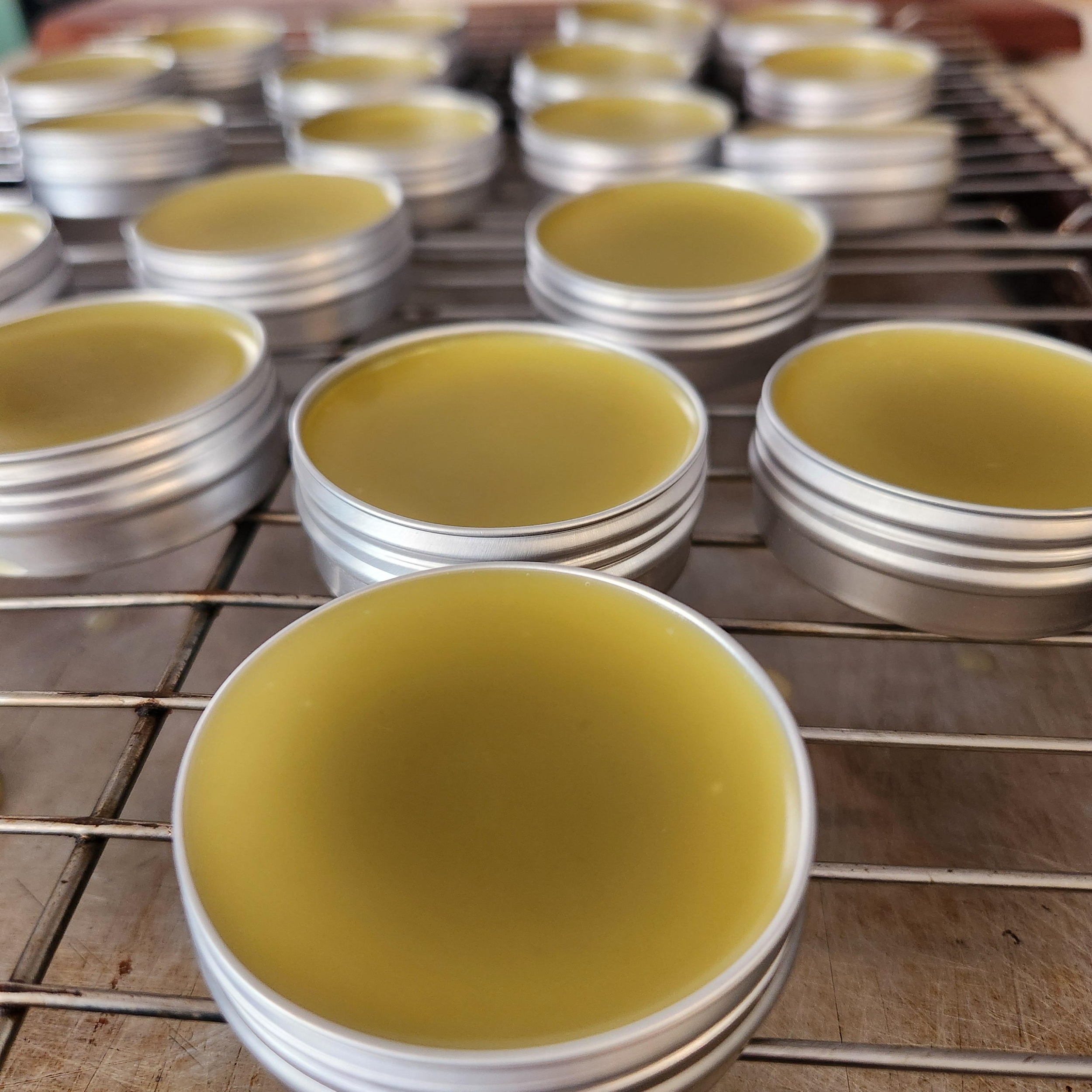 Stacks of small round metal tins filled with yellow substance, organized on a wire rack on a wooden surface.