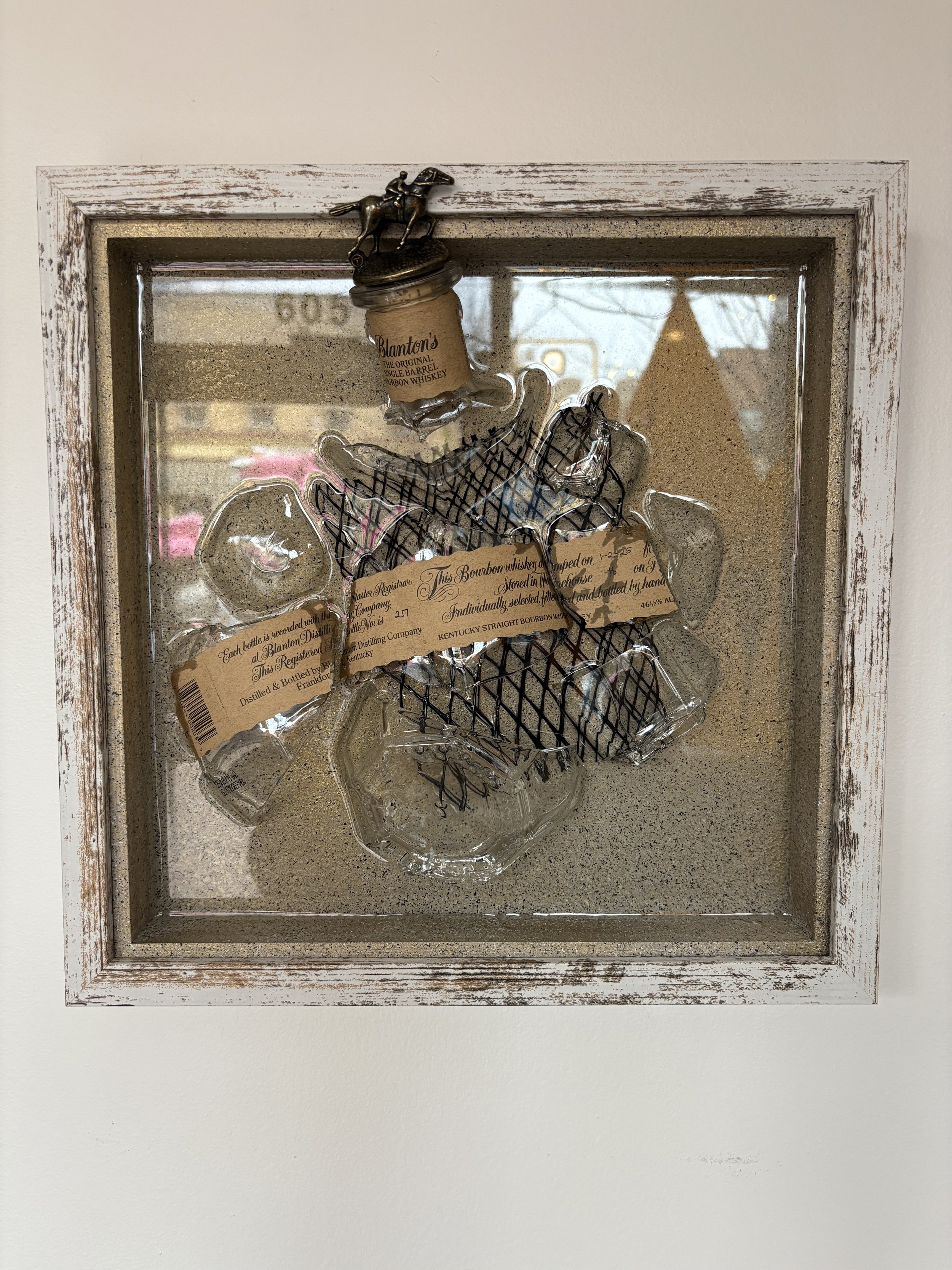 Wall-mounted display case with vintage whiskey labels and glass bottles, featuring a small metal horse statue on top.