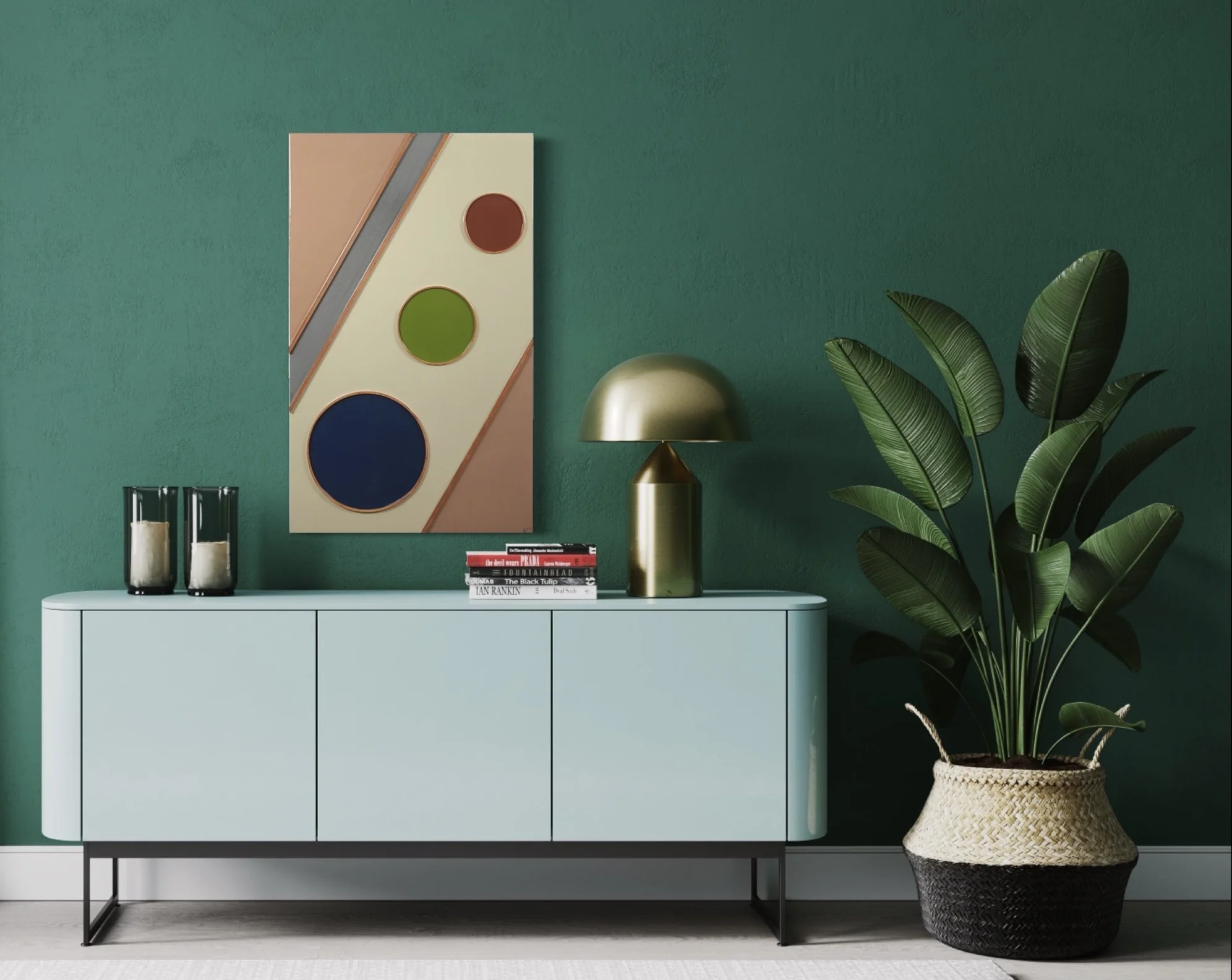 A modern light blue sideboard with black metal legs, decorated with a large potted plant with broad green leaves, a gold and black table lamp, a stack of books, and two black patternless vases with candles. A colorful abstract artwork hangs on a gree