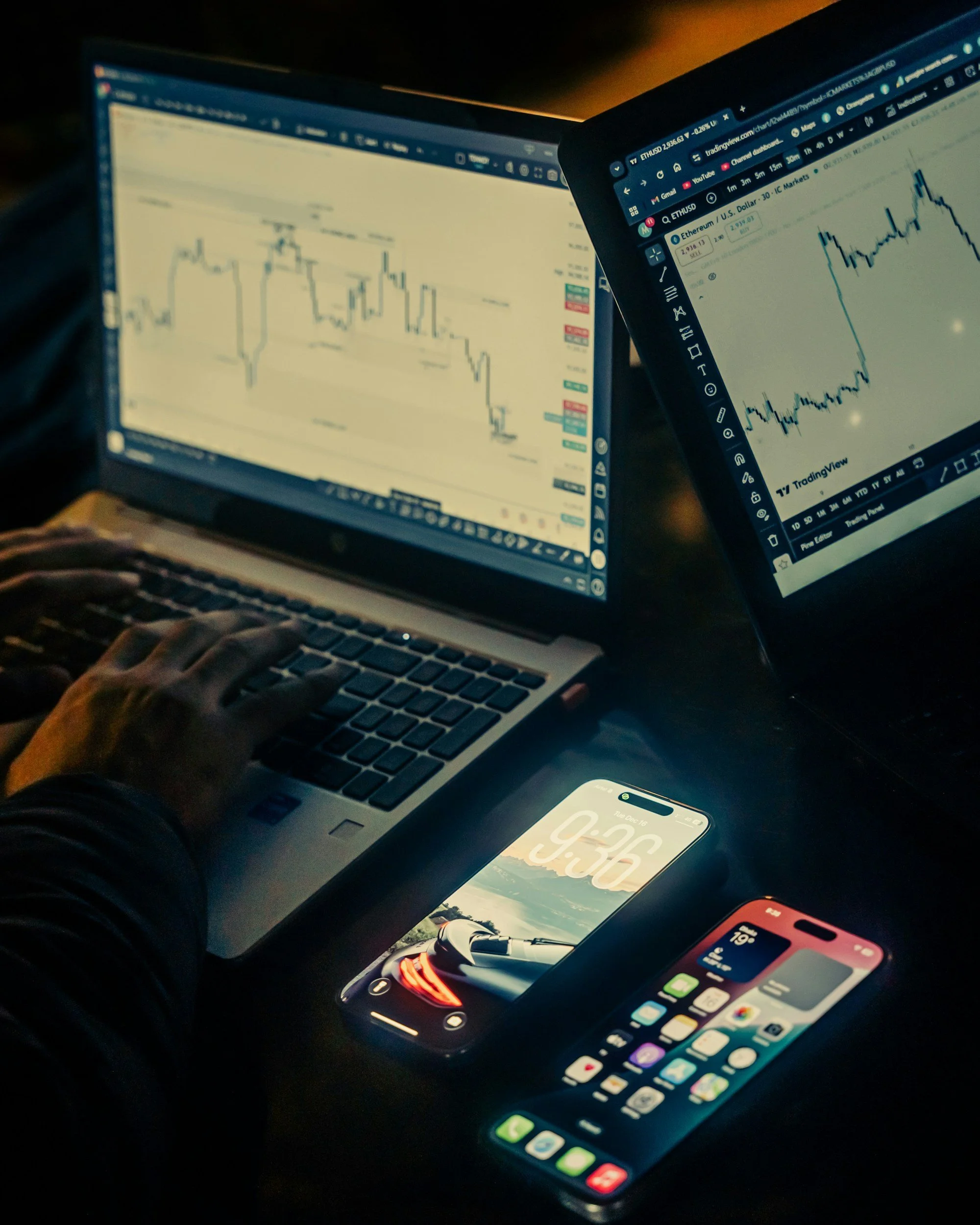 Two laptop screens showing financial charts, a smartphone with a landscape background and the time 9:36, and a tablet displaying a colorful app grid.