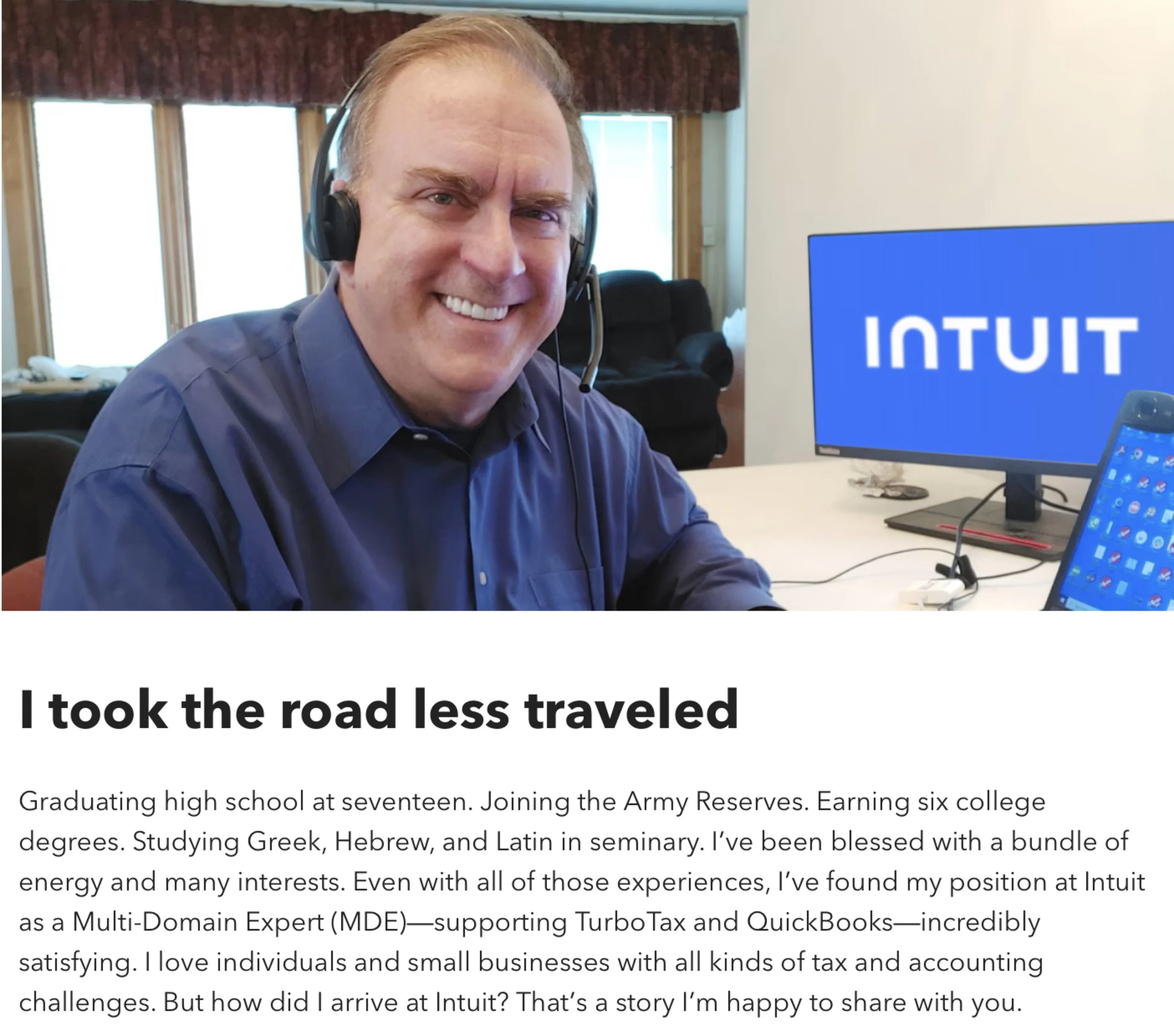 A smiling man with short hair, wearing a headset and a blue shirt, sitting in front of a computer monitor. The monitor displays the word 'INTUIT' in white letters on a blue background. Background includes windows with vertical blinds and a couch.