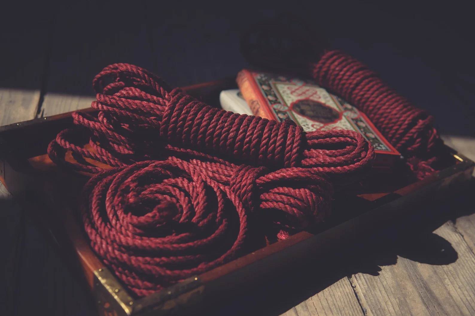 A tray containing red ropes and a set of playing cards with a decorative card back design, placed on a wooden surface.