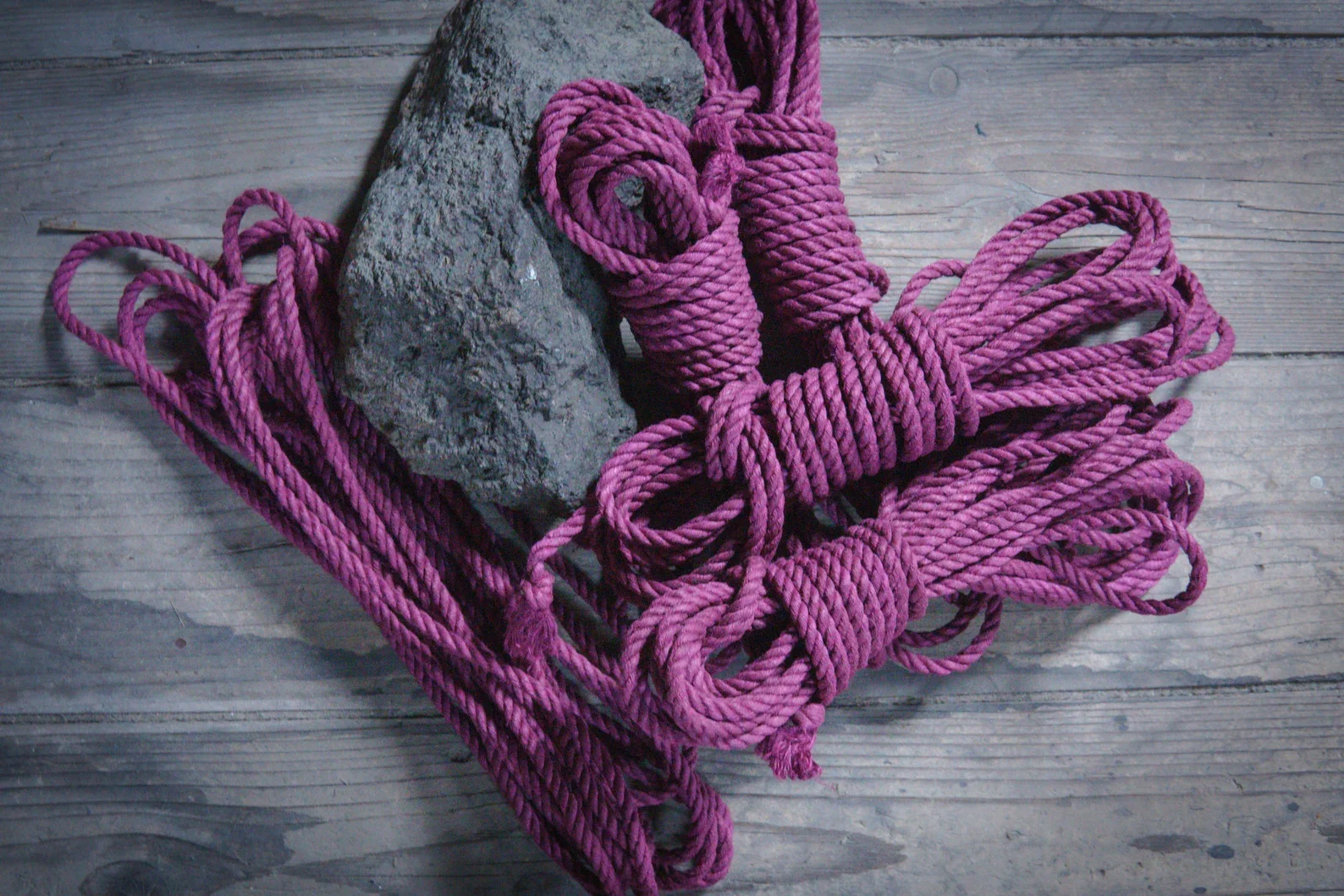 Pink climbing ropes and a gray rock on a weathered wooden surface.