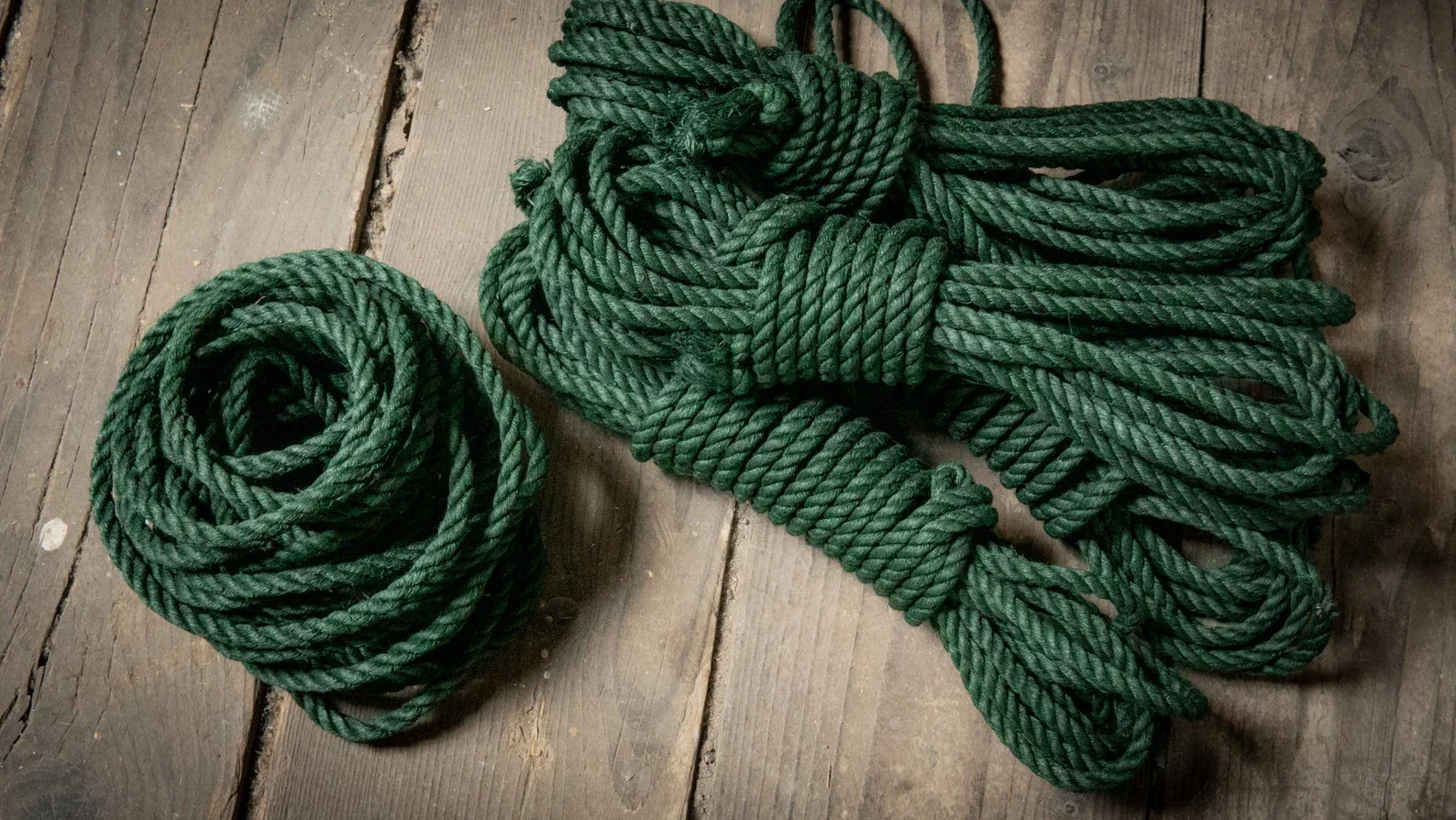 Green climbing rope coiled on a wooden surface.