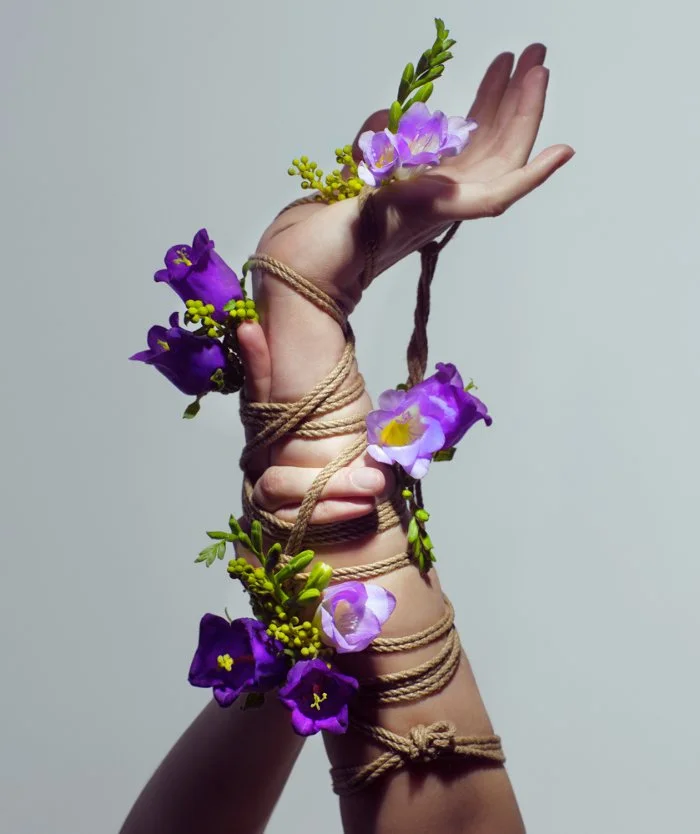 A person's hand and forearm wrapped in jute twine, decorated with purple and yellow flowers.