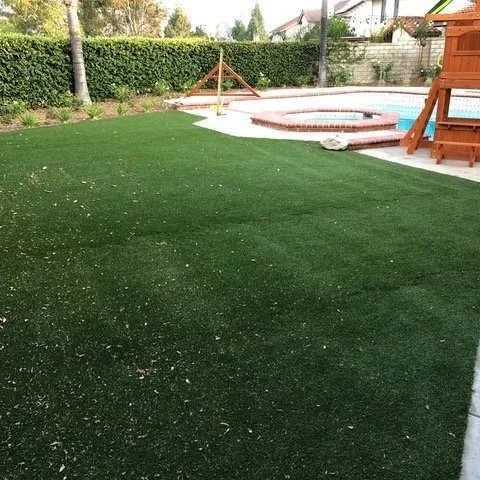 Residential backyard with a large artificial grass area, a hot tub, a wooden swing set, and a wooden playhouse.