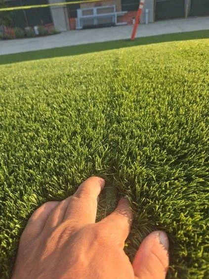 Green artificial turf with failing seam, hand opening turf to reveal failed seam