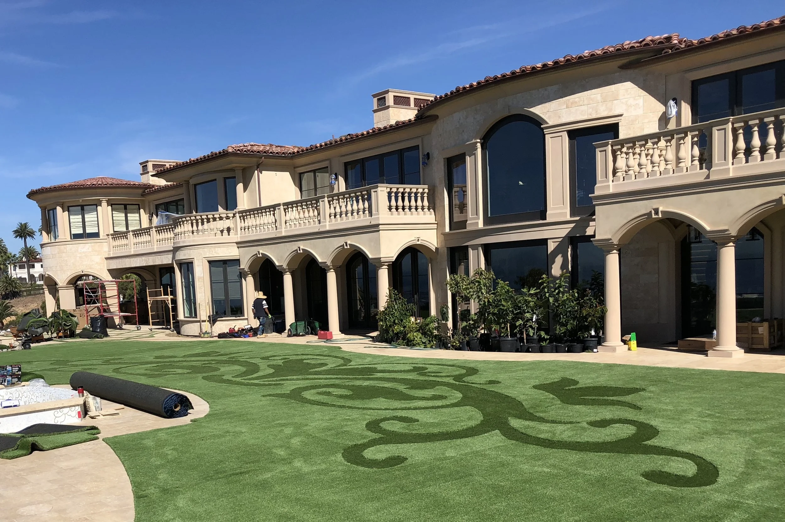 Green artificial turf with darker green artificial turf inlay design in front of custom Mediterranean styled home