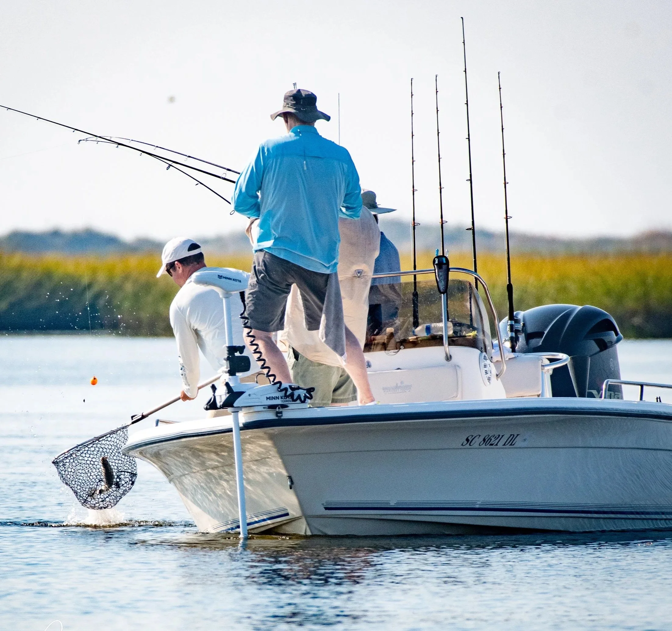 A group of people on a boat fishing on a body of water in a sunny outdoor setting.