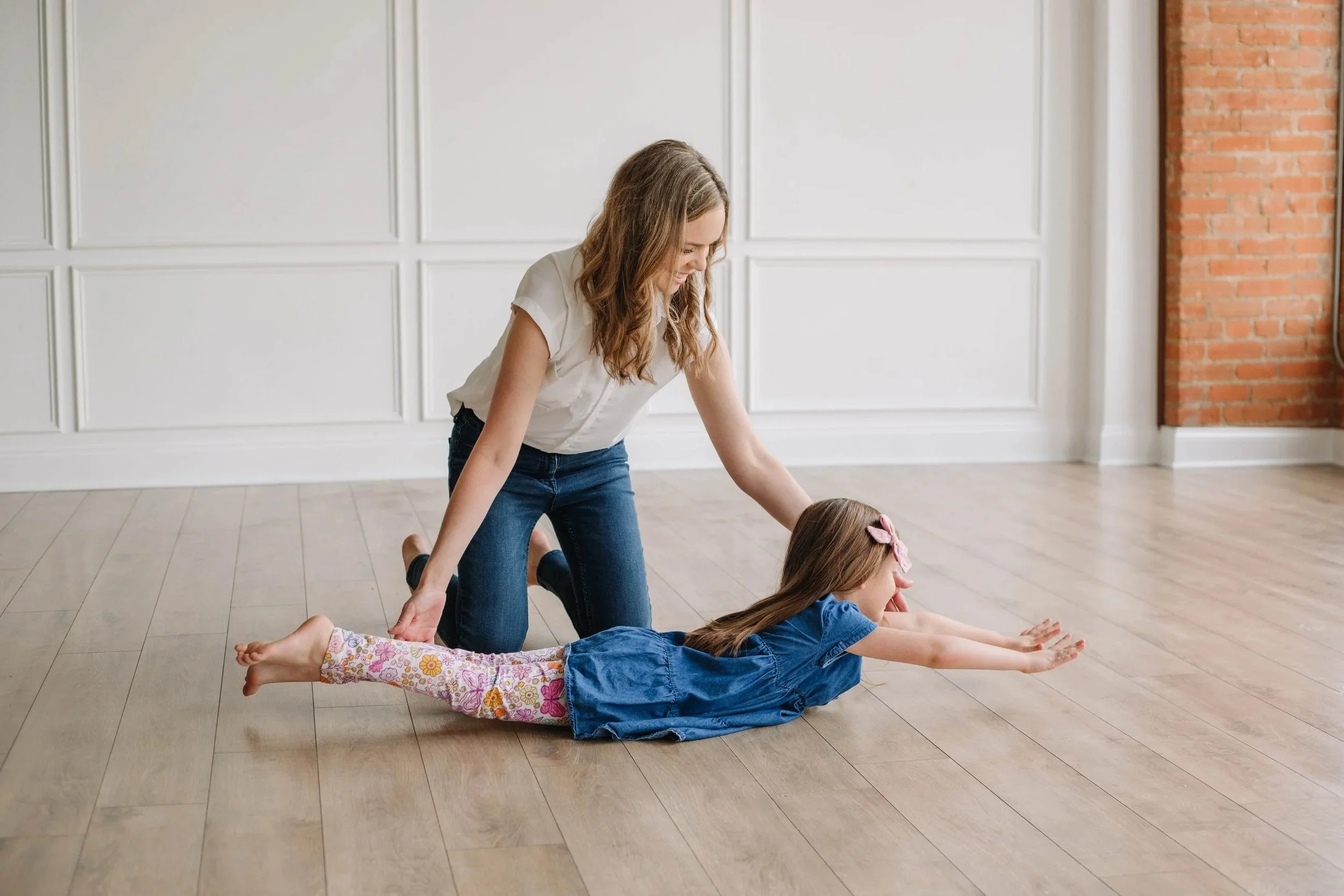 An occupational therapist sitting on her knees next to a young girl laying on the floor, working on integrating primitive reflexes during occupational therapy for children in Dallas, TX