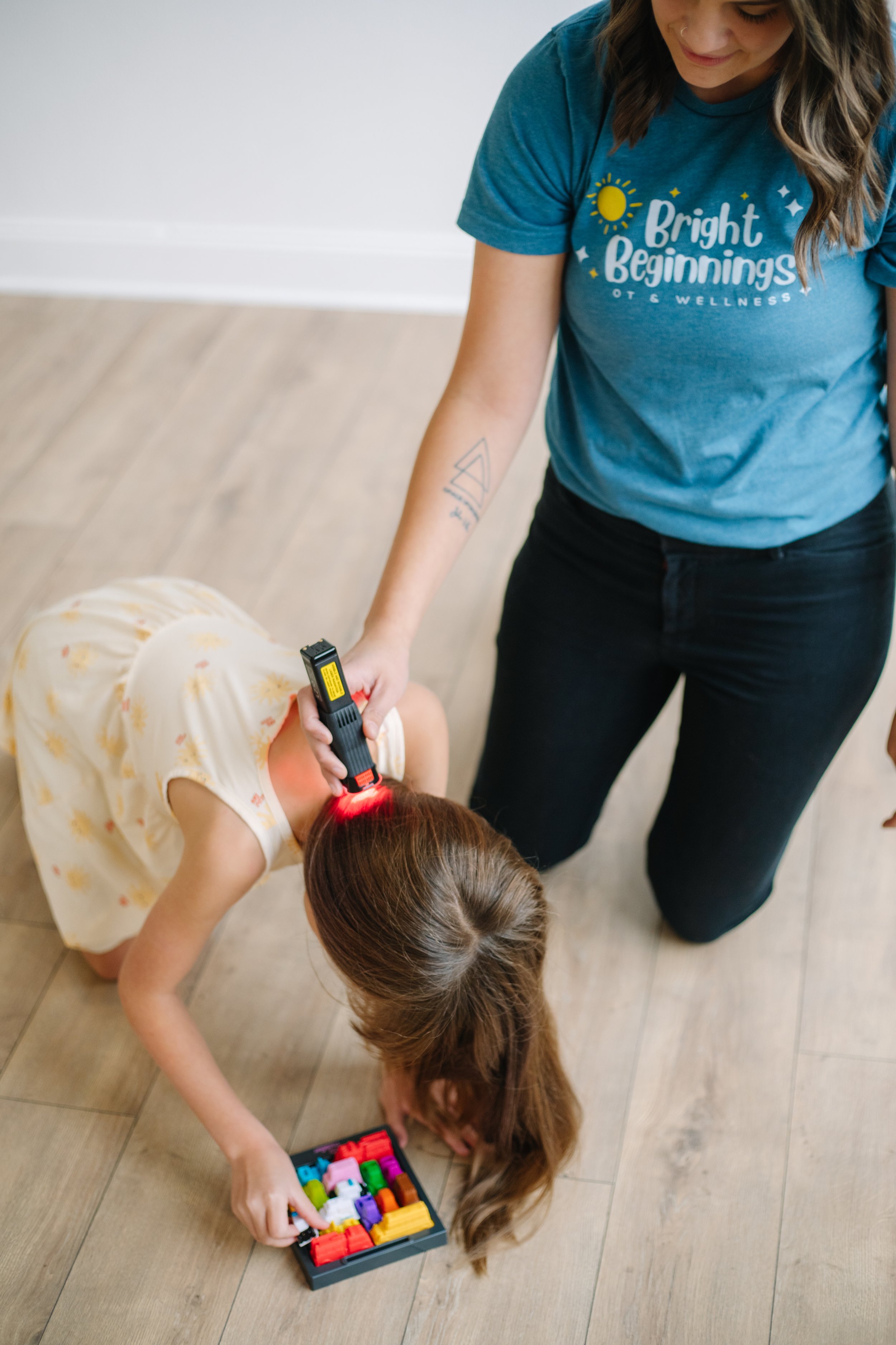 An occupational therapist in Dallas, TX providing low-level laser light therapy to a child to help with emotional regulation and sensory processing while the child plays with blocks on the floor
