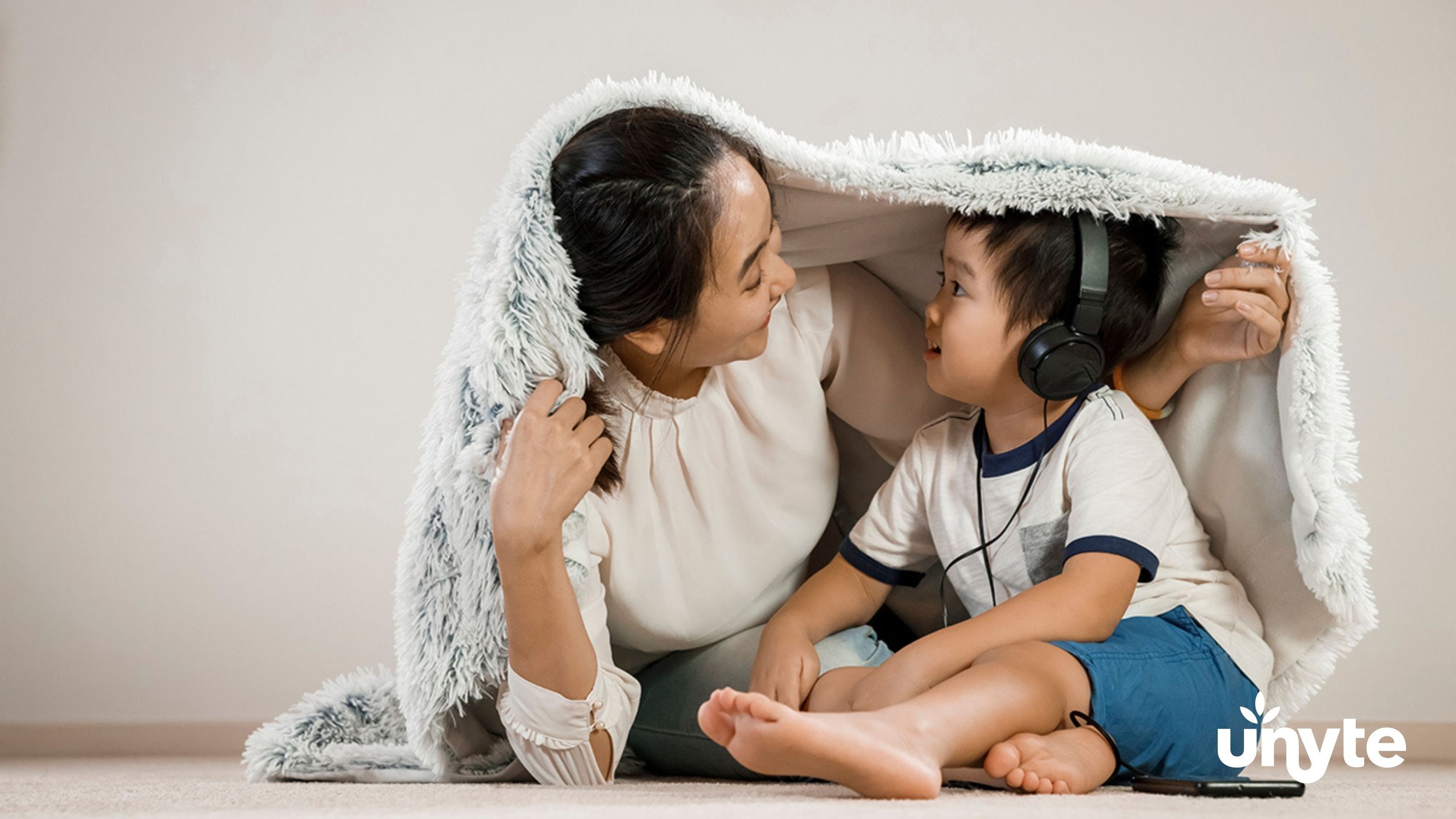 A young boy wearing headphones, relaxing with his mom in a blanket fort, participating in The Safe and Sound Protocol (SSP) in Dallas, TX - an evidence-based listening therapy designed to help regulate the nervous system.