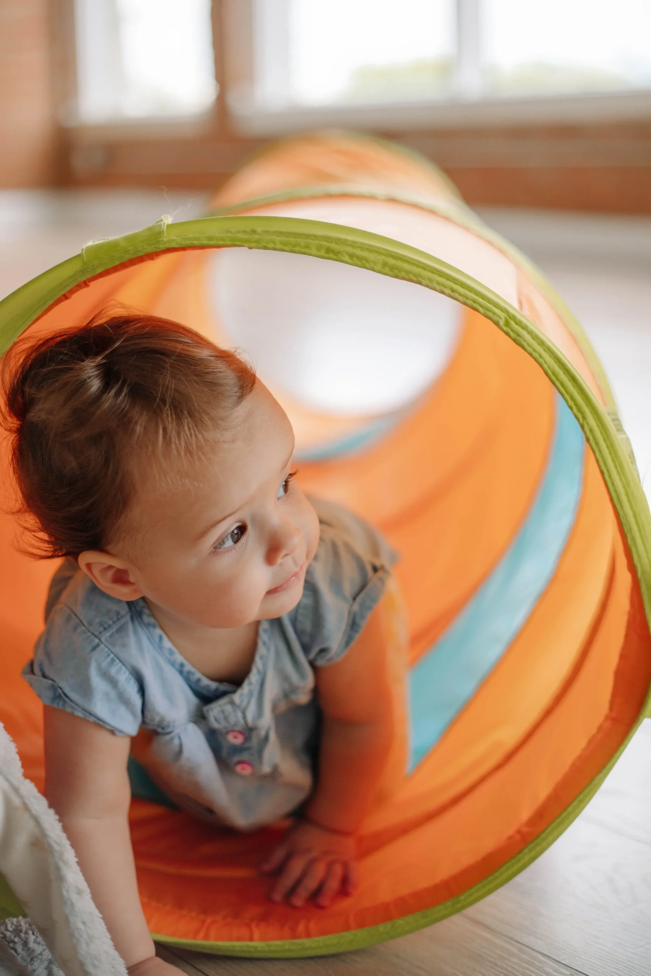 A young child with brown hair crawling through a play tunnel during occupational therapy for developmental skills in Dallas, TX
