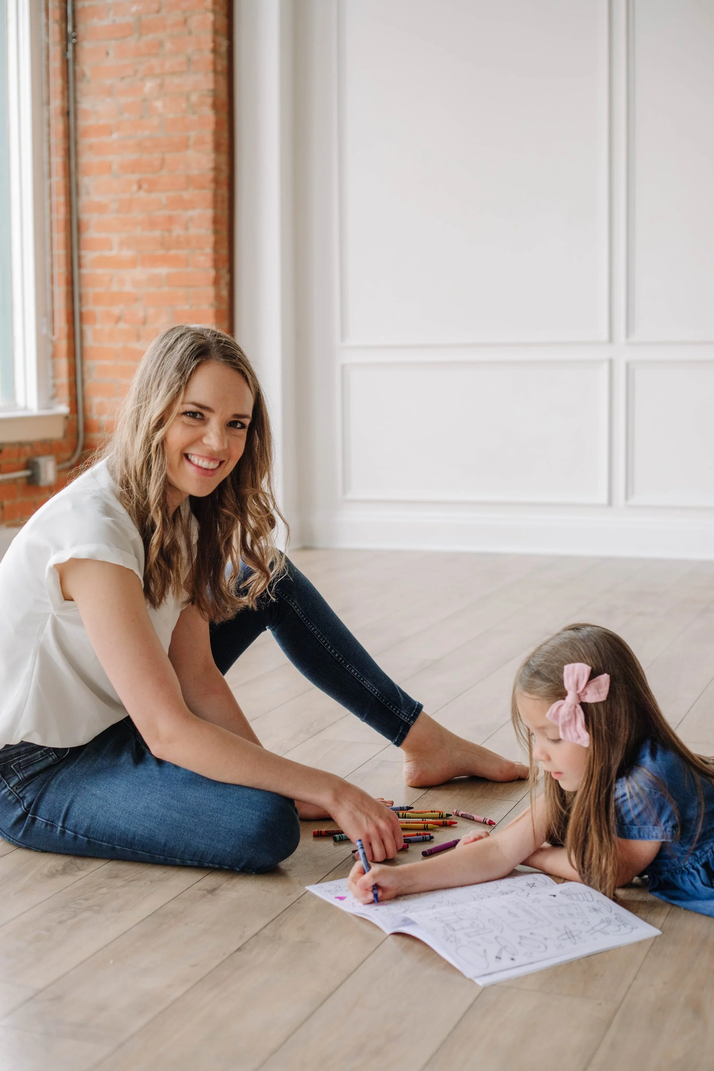 A pediatric occupational therapist is sitting on the floor next to a child who is lying on the floor coloring with crayons, working on fine motor skills during occupational therapy for kids in Dallas, TX.