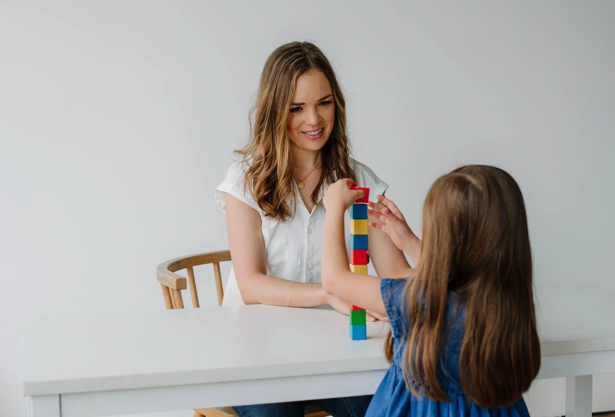 An occupational therapist sitting at a table with a school-age girl, working on stacking blocks for motor skill improvement during OT for kids in Dallas, TX
