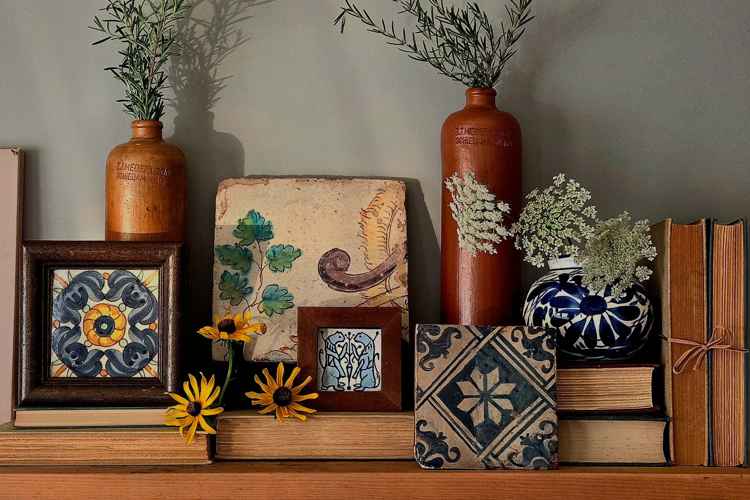 A collection of decorative items including framed artwork, ceramic vases with greenery, books, and flowers arranged on a shelf.