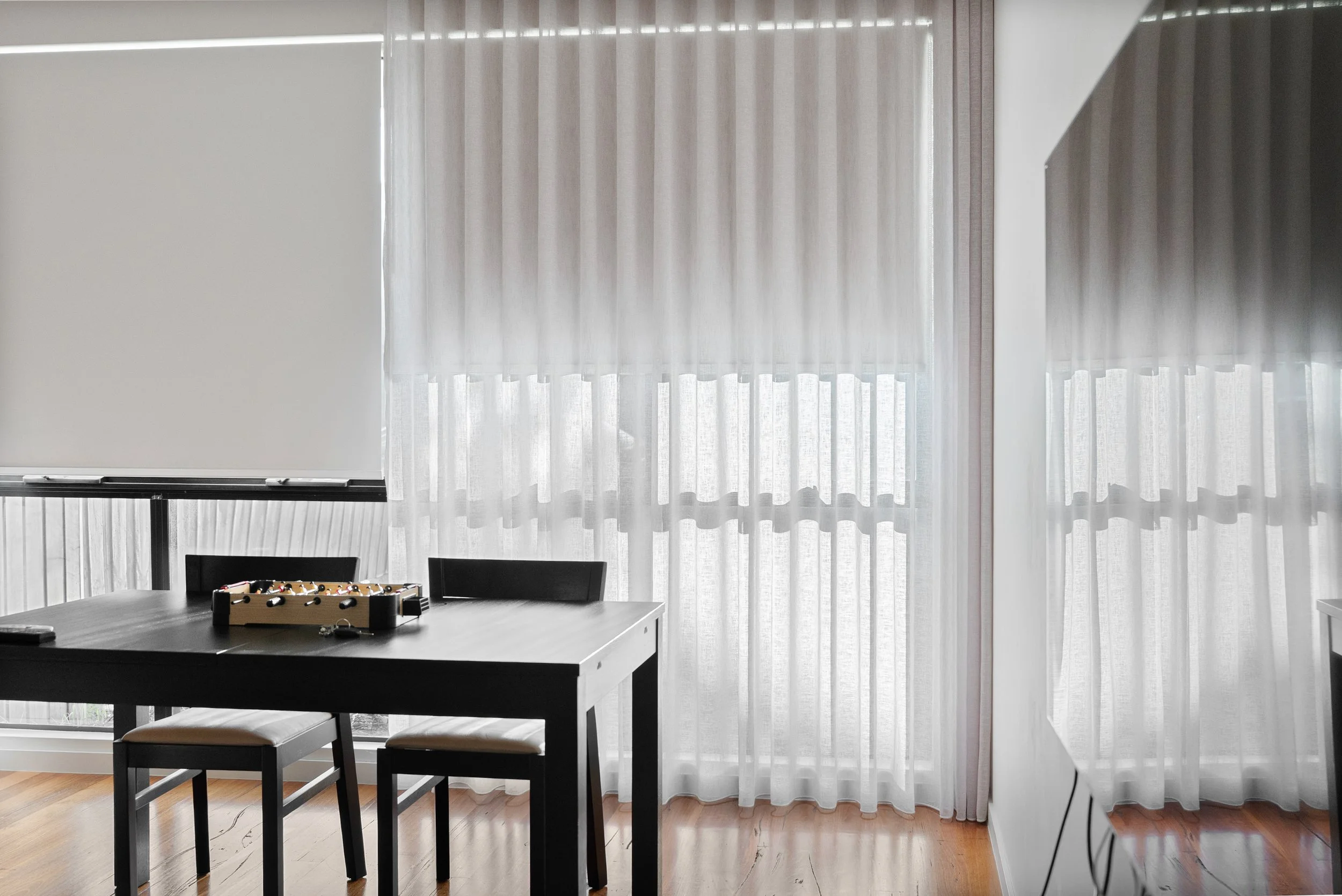 Dining table with sheer curtains closed and a roller blind lowered beside them
