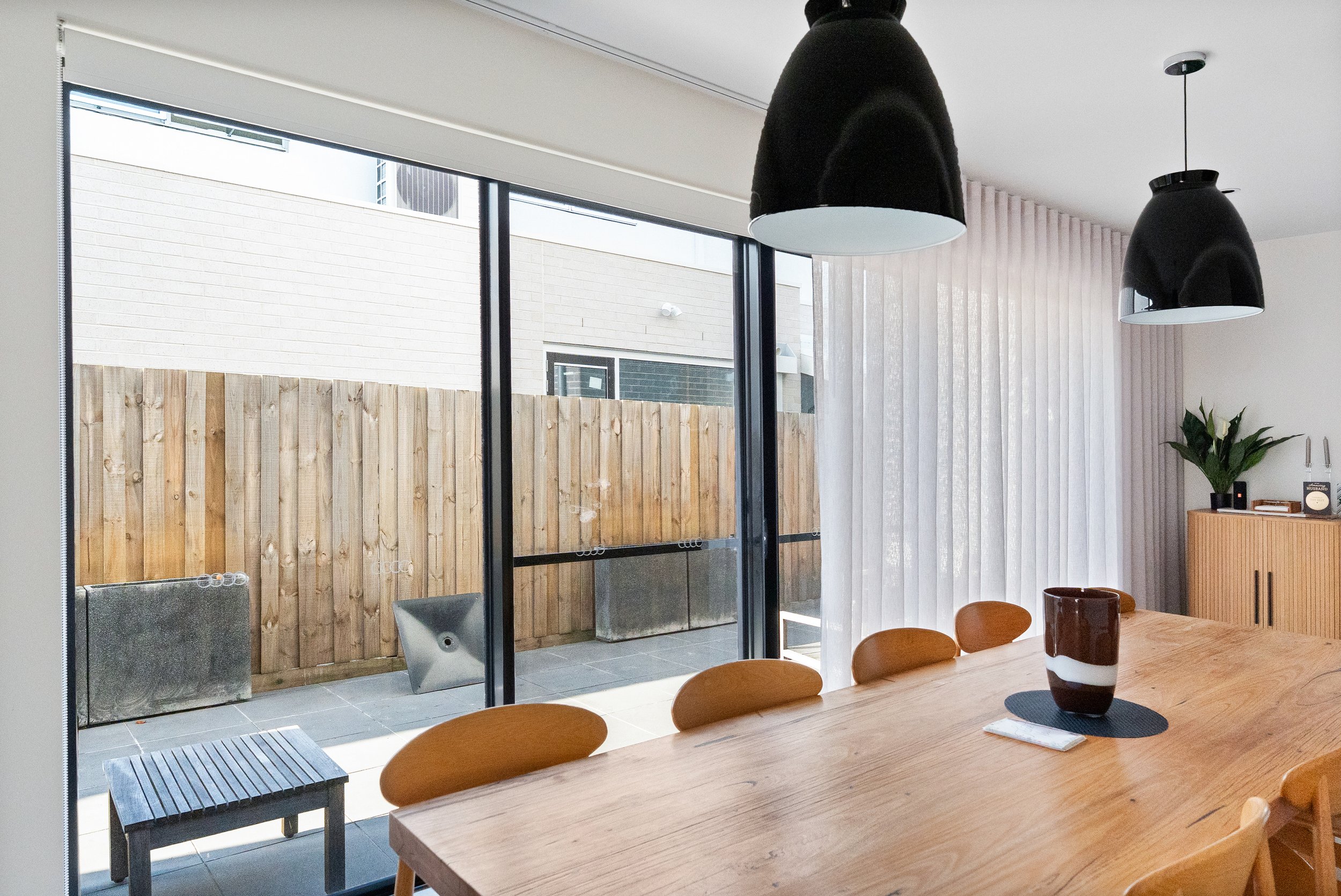 Dining table beside open sliding doors, with sheer curtains stacked to one side