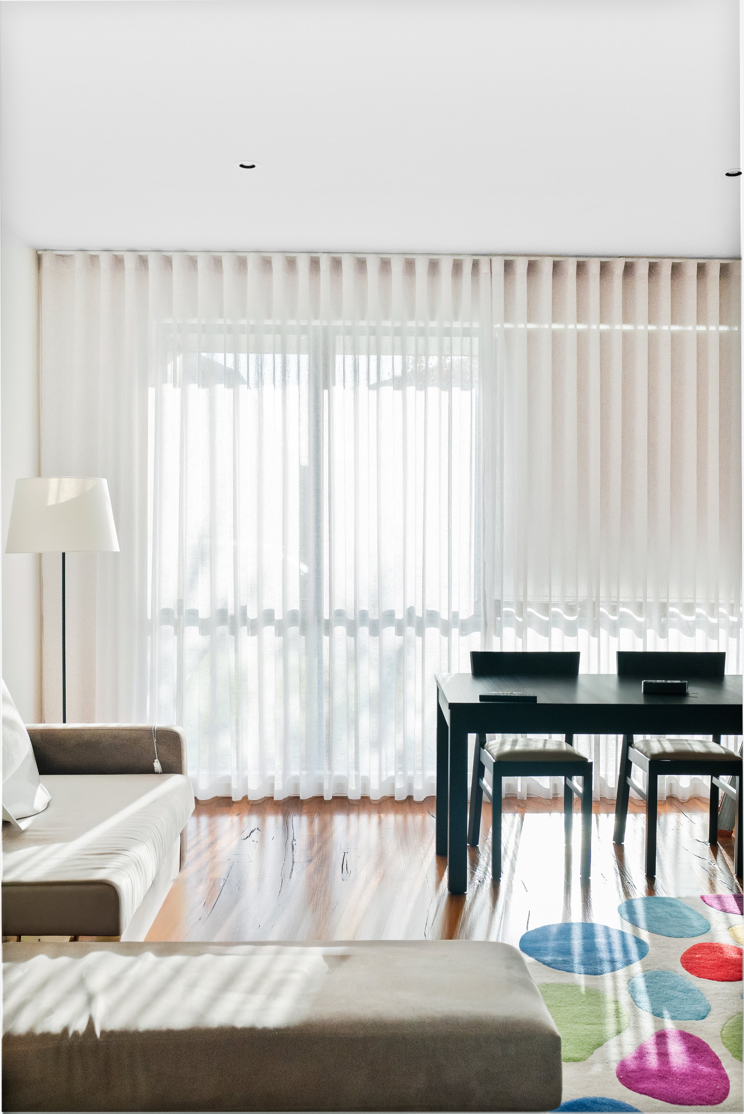Sheer curtains across a living room window, behind a sofa and dining table