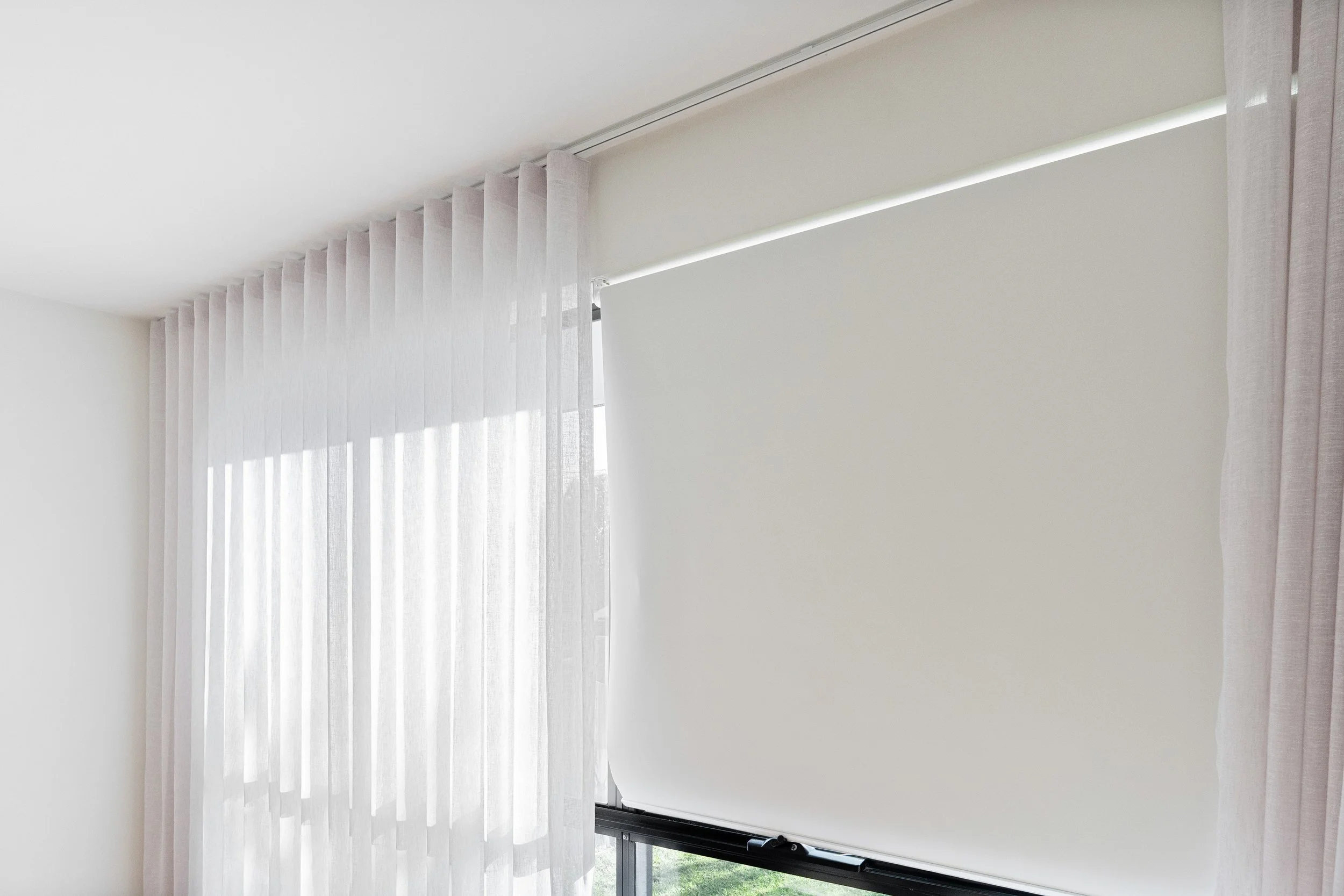 Close-up of a roller blind lowered beside a sheer curtain