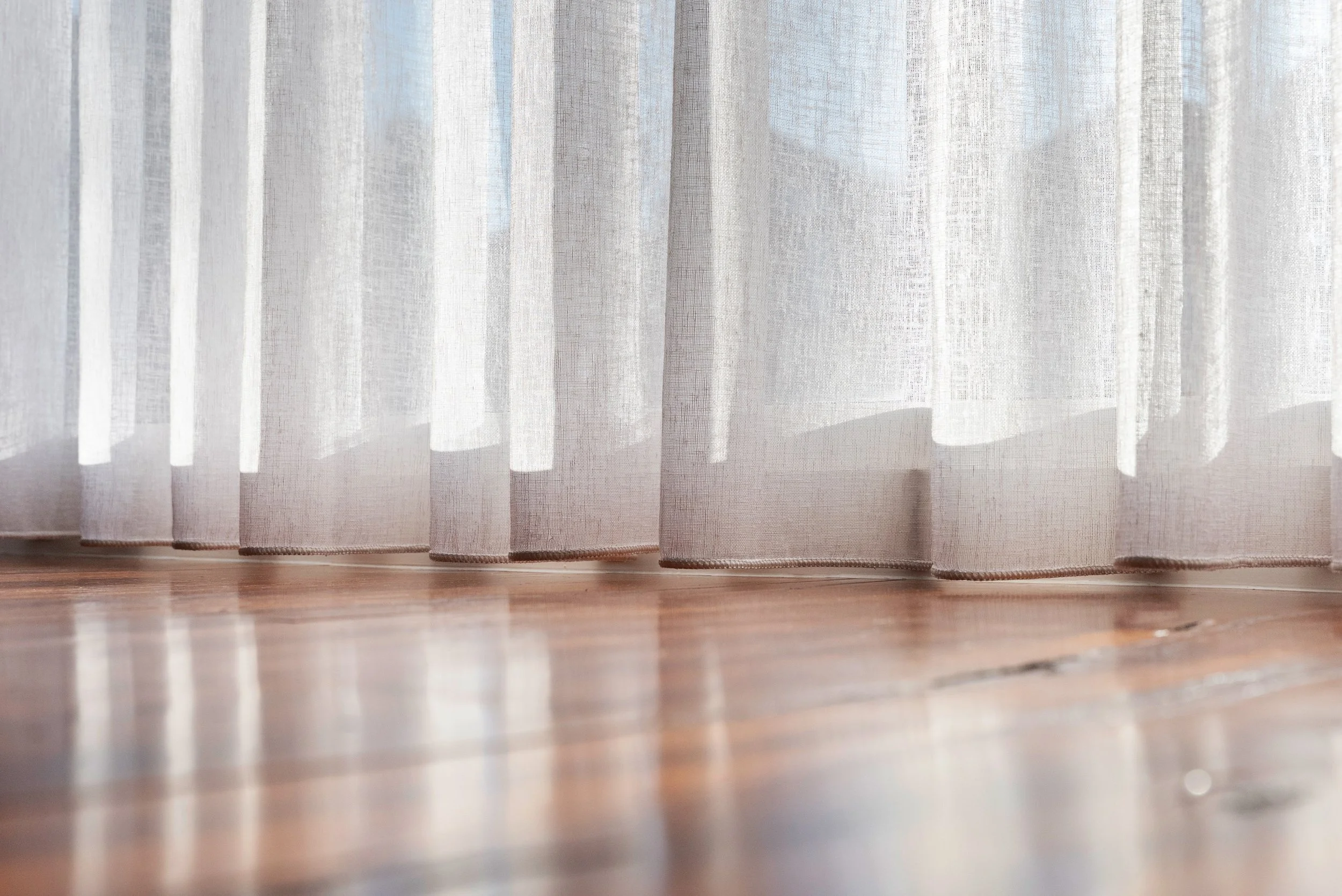 Sheer curtain hems sitting just above a polished timber floor