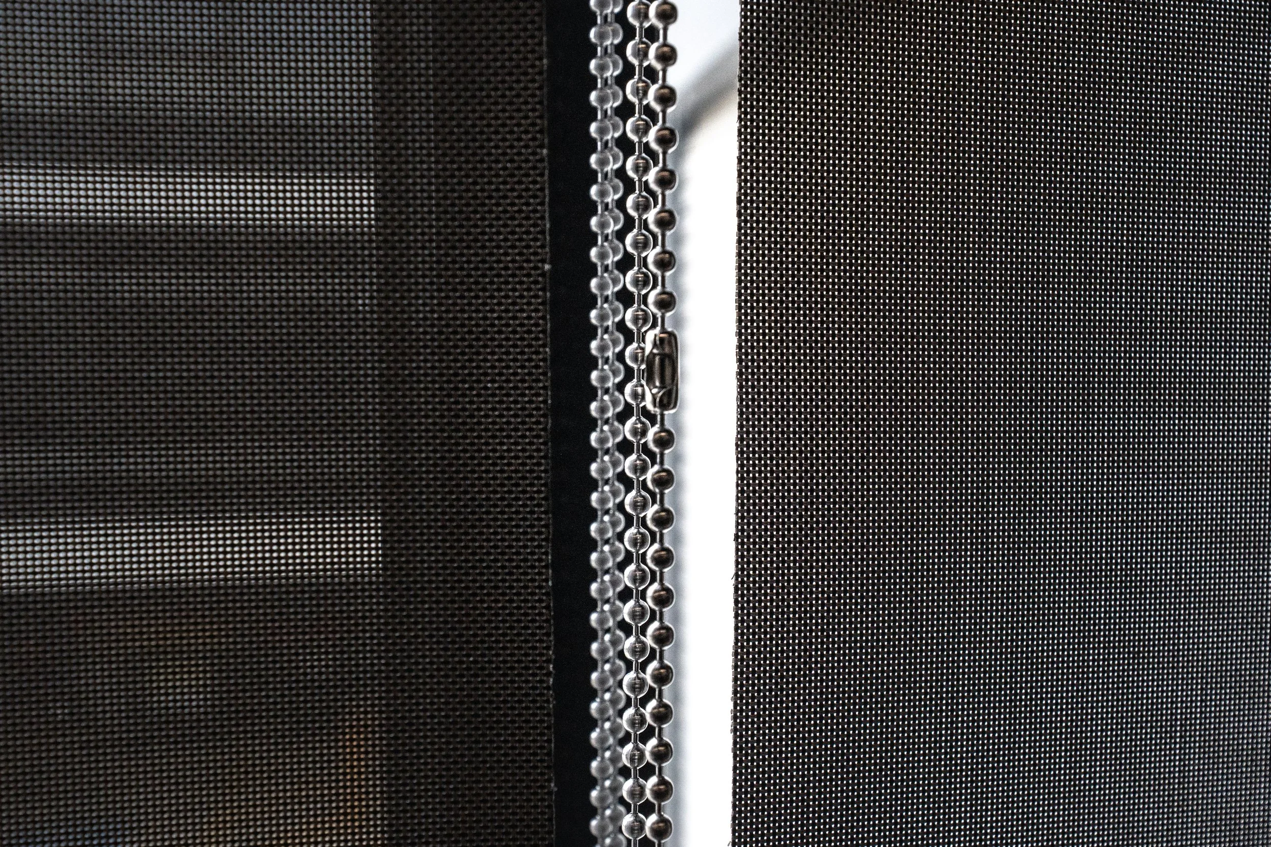 Close-up of sunscreen blind fabric and the control chains between two blinds