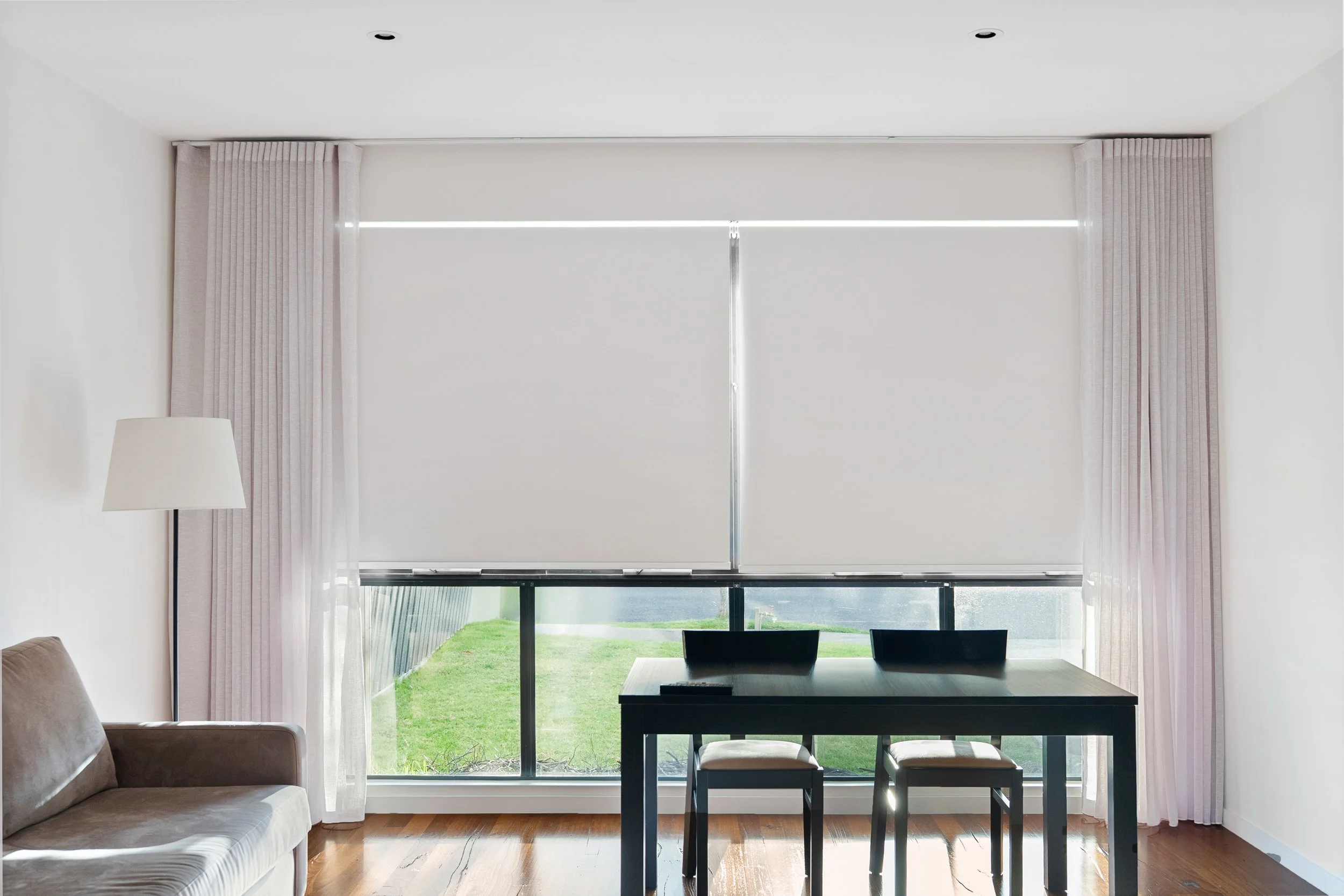 Two roller blinds lowered over a wide window, with curtains stacked either side