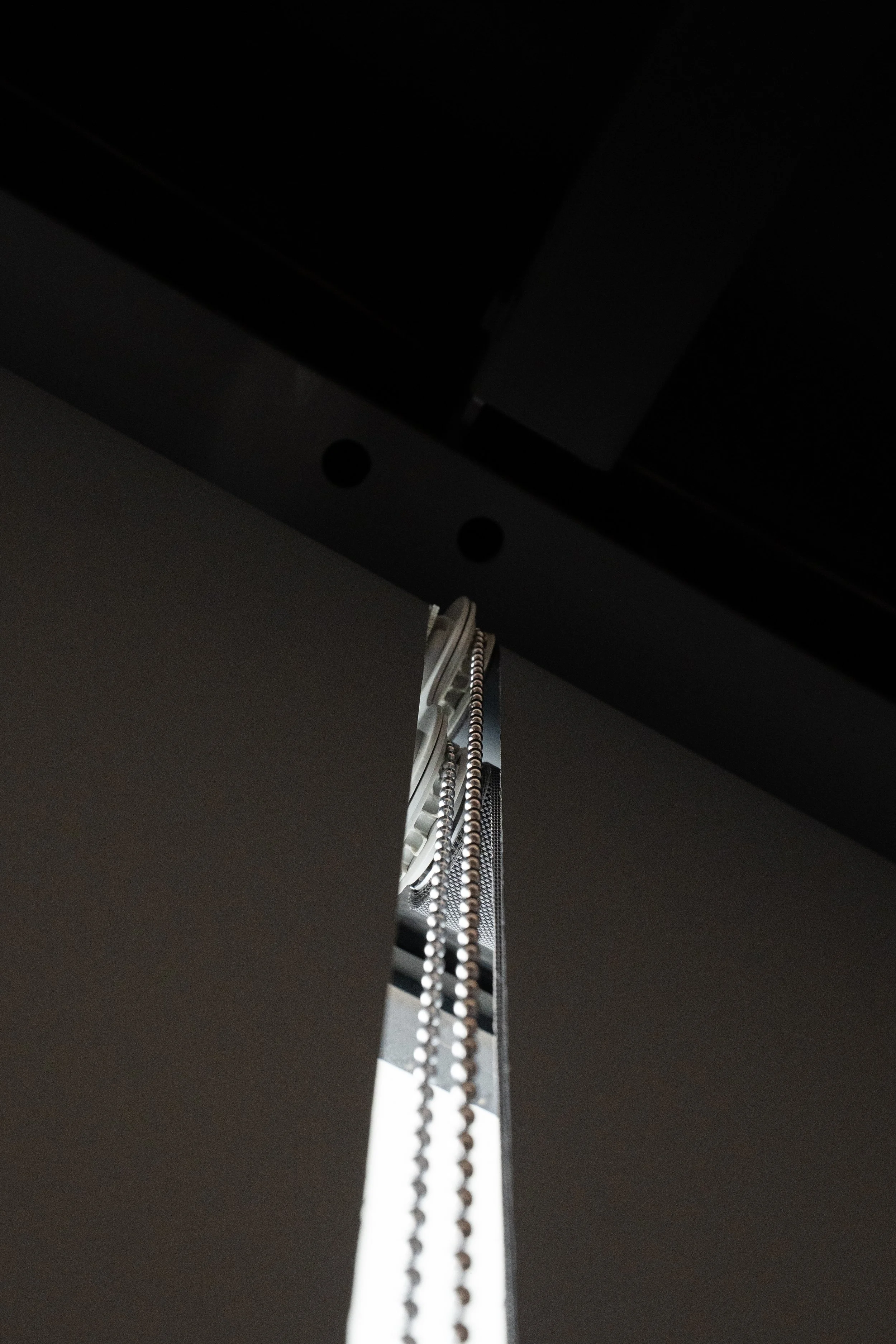 Top corner of a dark roller blind with its control chain