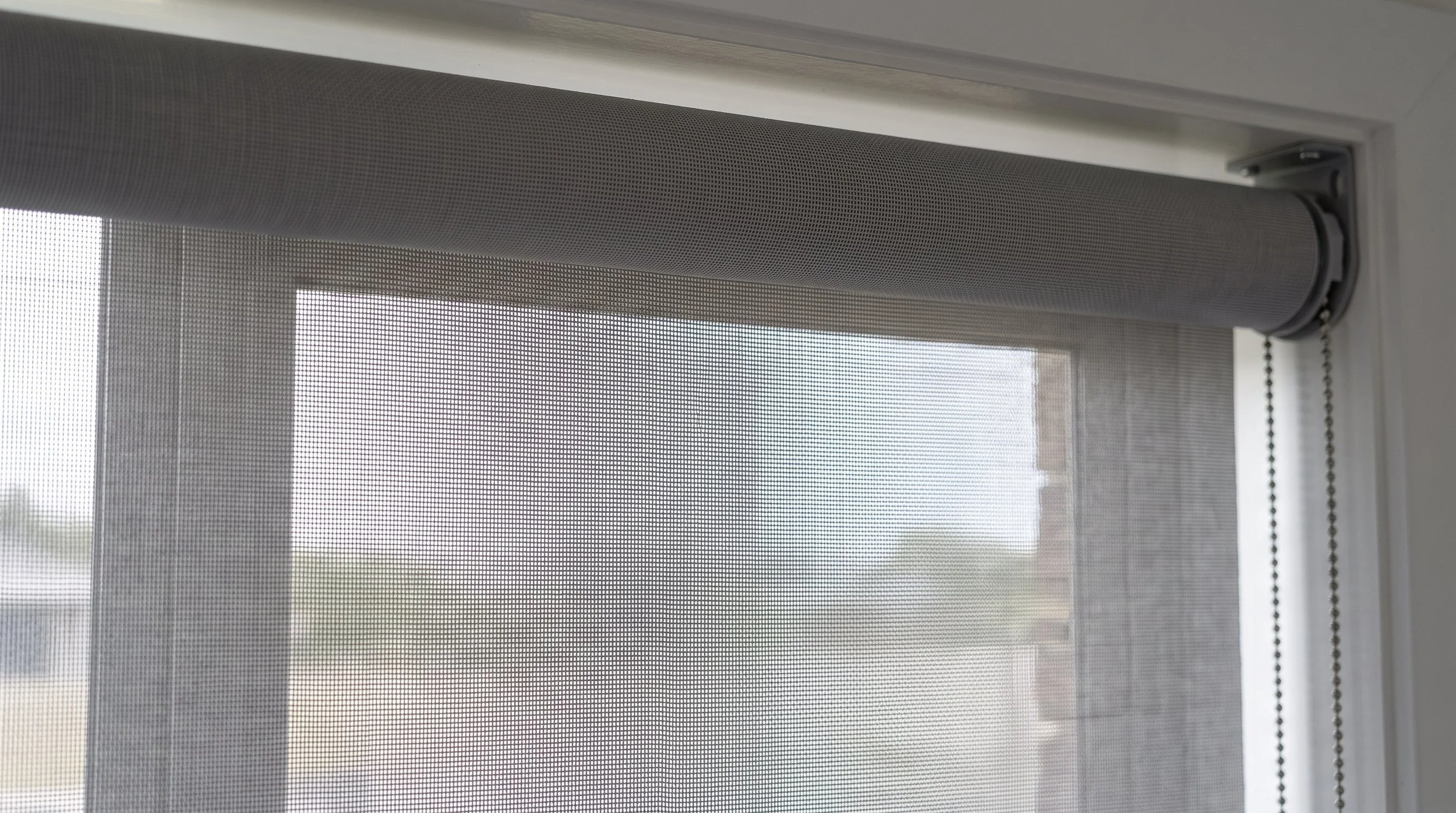 Reverse-roll sunscreen roller blind with the fabric dropping close to the glass