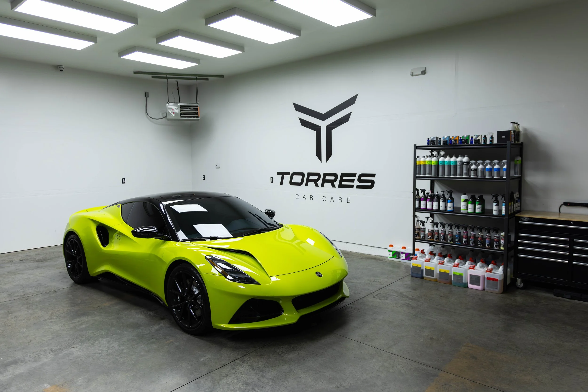 Interior of a car care shop with a yellow sports car, a large Torrees Car Care logo on the wall, and shelves of car cleaning supplies.