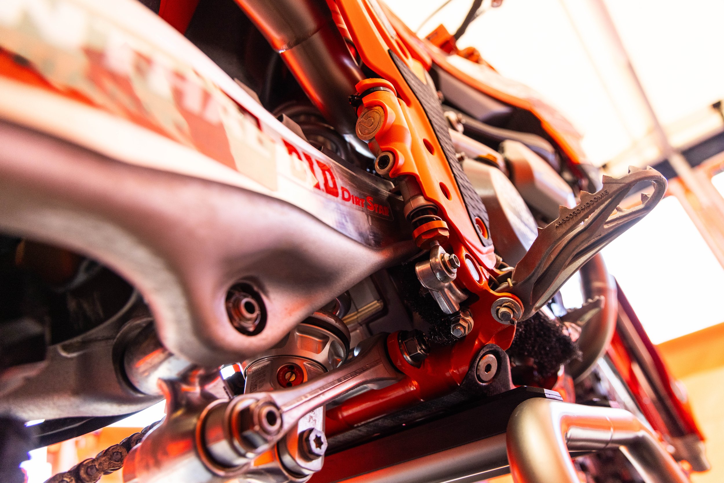 Close-up of the chain, driver, and orange suspension components of a dirt bike.