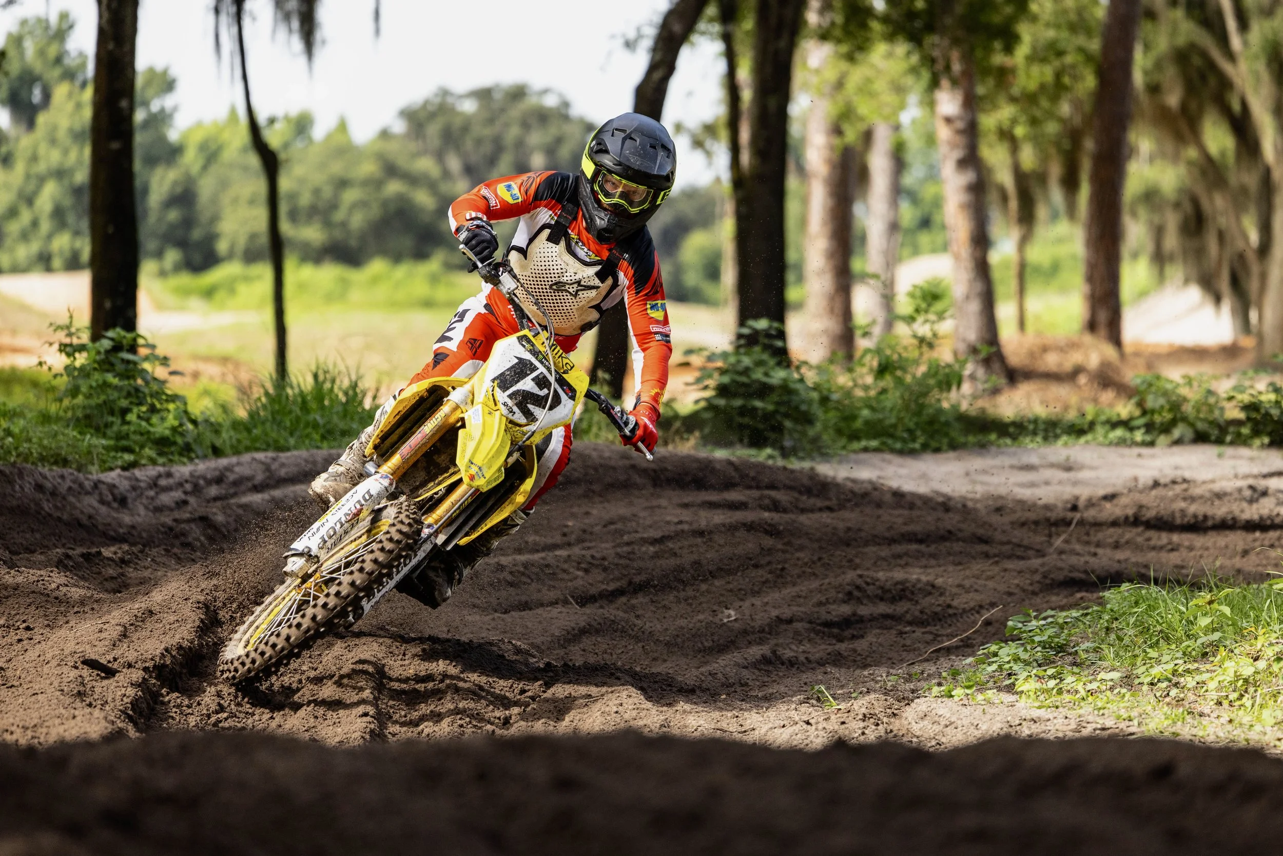 Motocross rider in full gear riding a dirt bike through a forest trail, kicking up dirt.