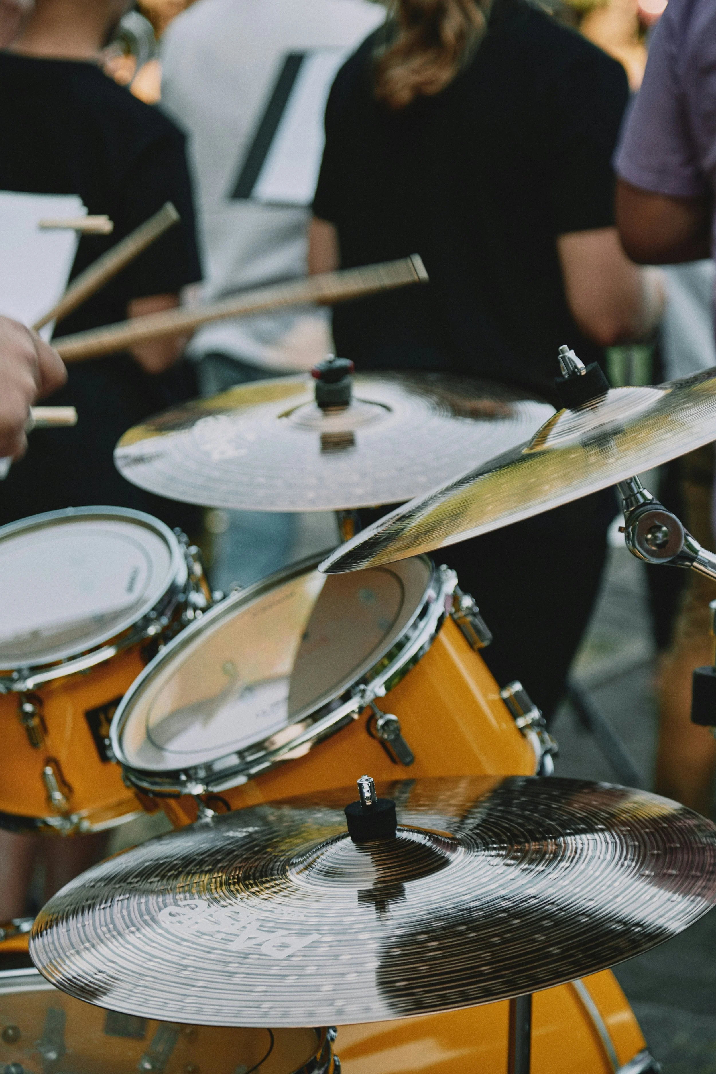 Close-up view of a yellow drum set and various cymbals being played by musicians at an outdoor event.