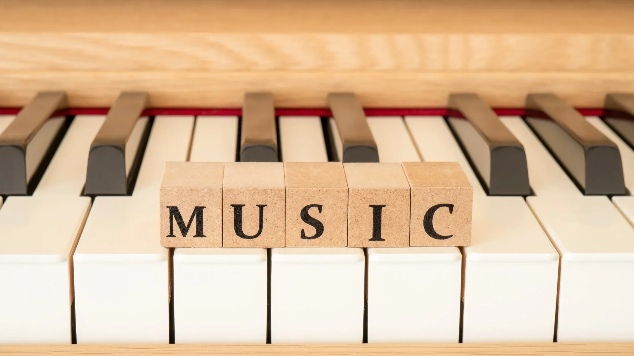 Close-up of piano keys with wooden blocks spelling out 'MUSIC' placed on the keys.