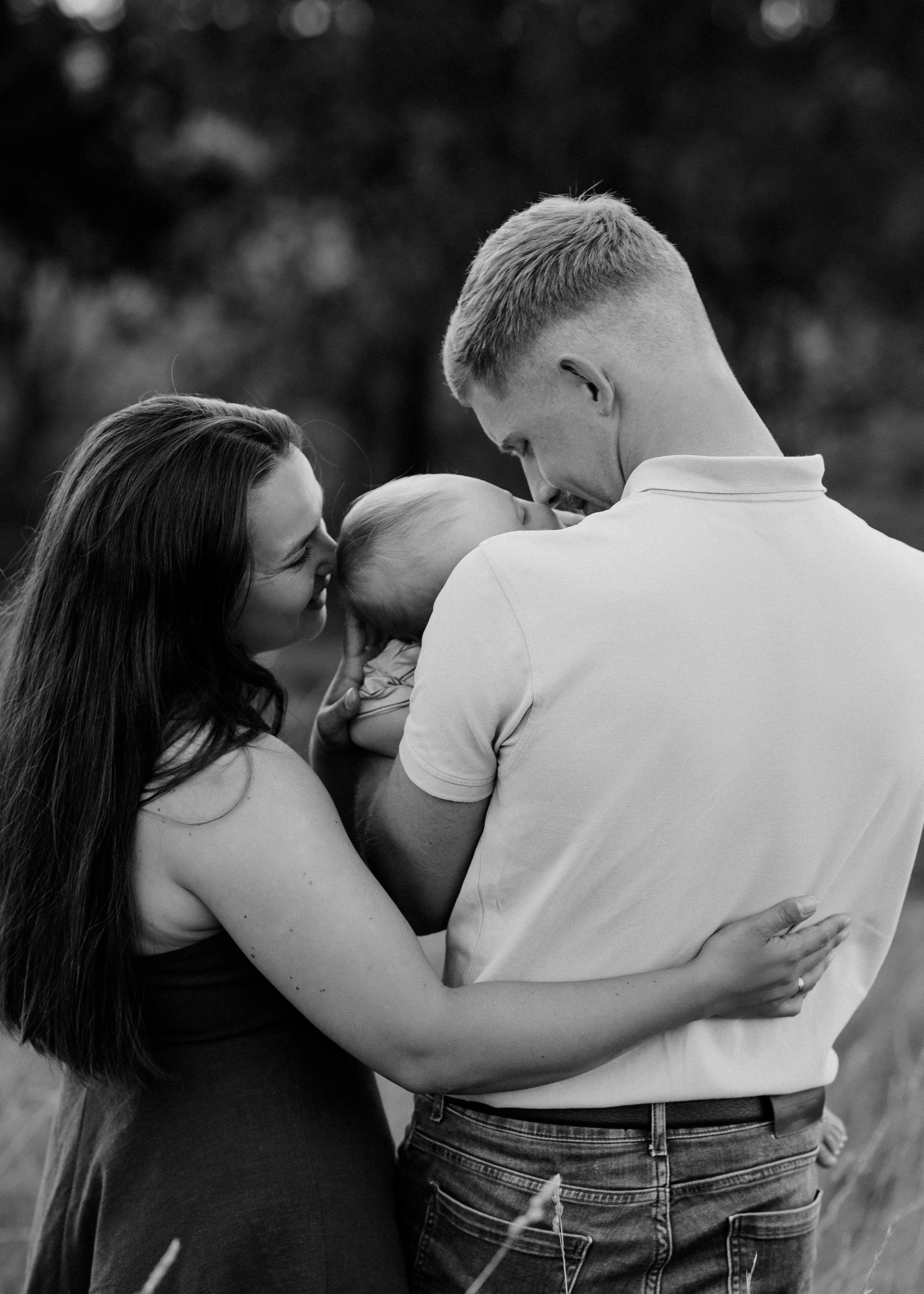 A black-and-white photo of a family embracing outdoors, with two women and two men holding a baby.