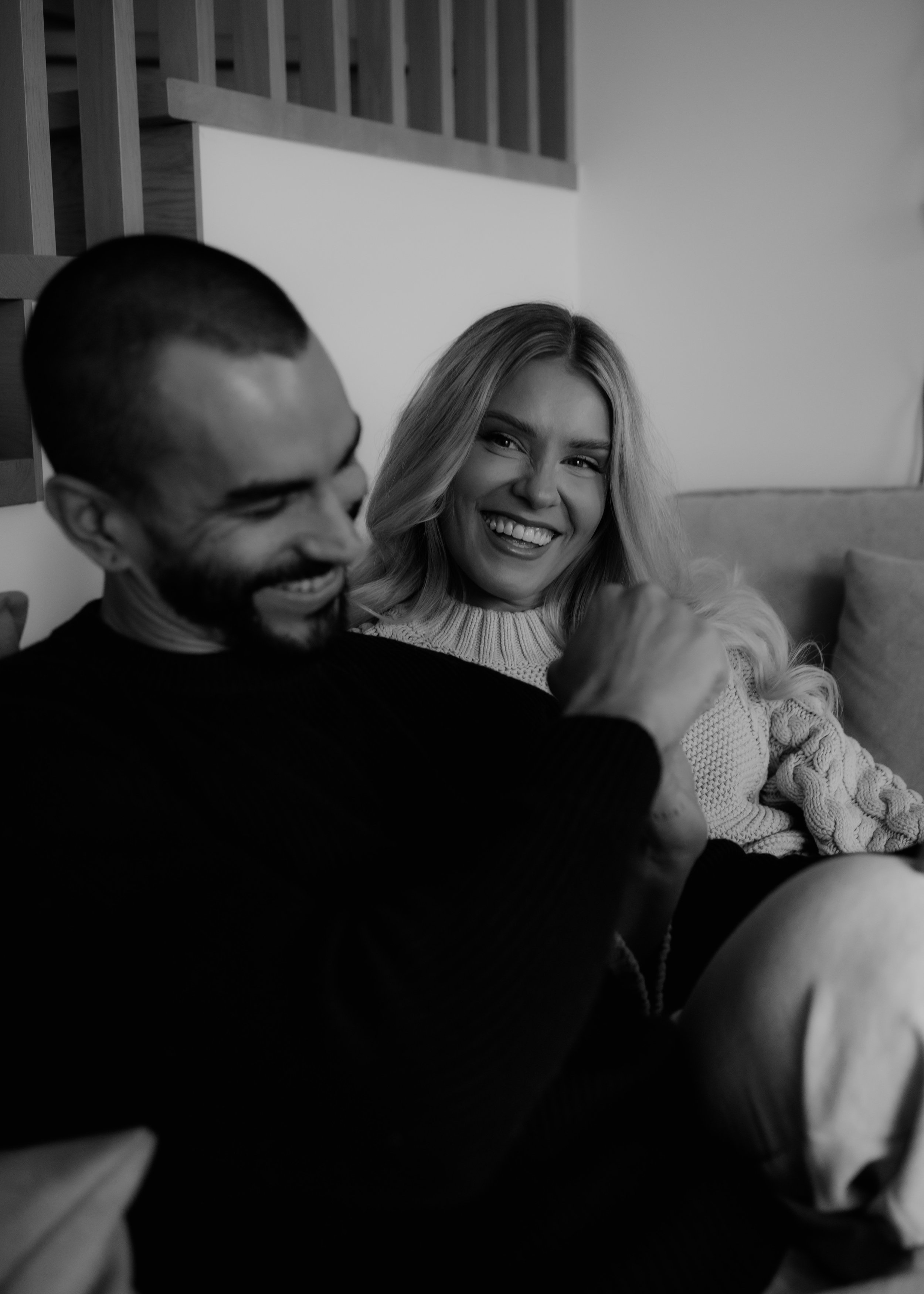 Black and white photo of a smiling woman with long hair and a man with short hair, both sitting close together on a couch.
